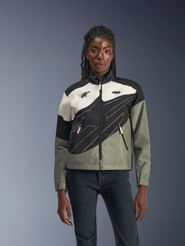 Mulher a usar o Casaco Alpinestars Stella Moshell, casaco de motociclismo urbano em Preto, Cinzento Fur Gray, Off White e Rosa, design assimétrico com grafismos técnicos, puxadores de fecho rosa e logótipos Alpinestars, estilo streetwear contemporâneo para condutoras urbanas.
