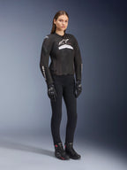 Female rider wearing the Alpinestars Stella T-GP Plus R V4 Airflow Jacket, Black and White, featuring mesh panels for ventilation and white logos, paired with black pants, black gloves, and black boots with pink accents, women's sport motorcycle riding gear