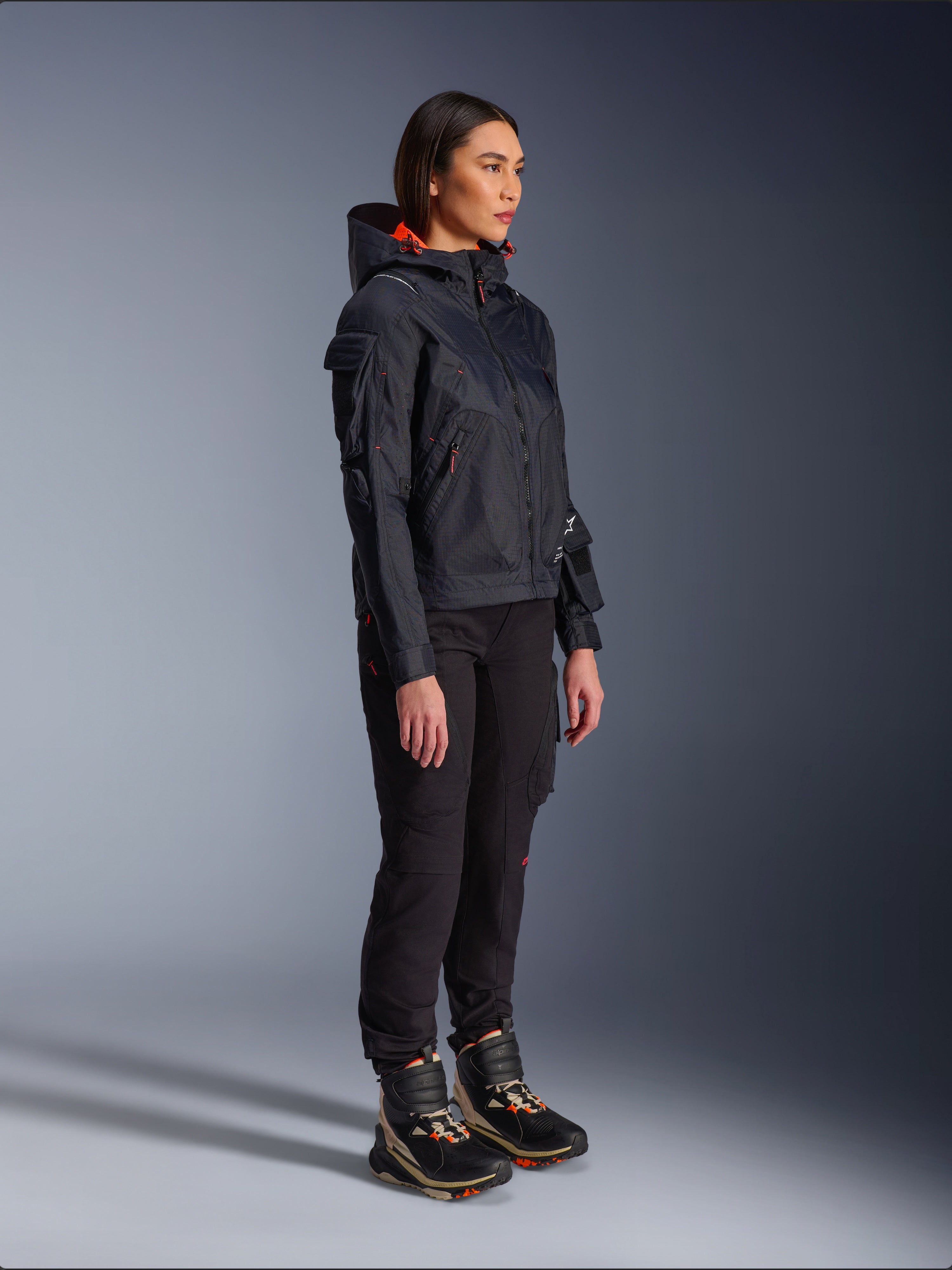 Alpinestars Actea Women's Pants in Black, regular fit with cargo pockets, styled with a black Molly Air Jacket with orange accents and high-top riding shoes, contemporary urban motorcycle apparel for women