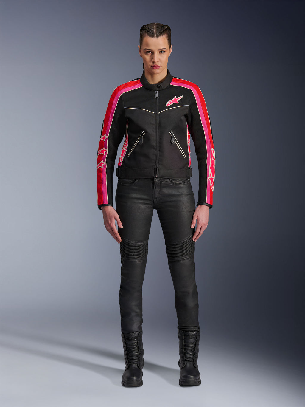 Female rider wearing the Alpinestars Stella T-Dyno Air Jacket, Black with Bright Red and Fuchsia accents, paired with black motorcycle pants and lace-up boots, featuring 3D mesh panels, tailored fit, and pink star logos, urban riding gear outfit