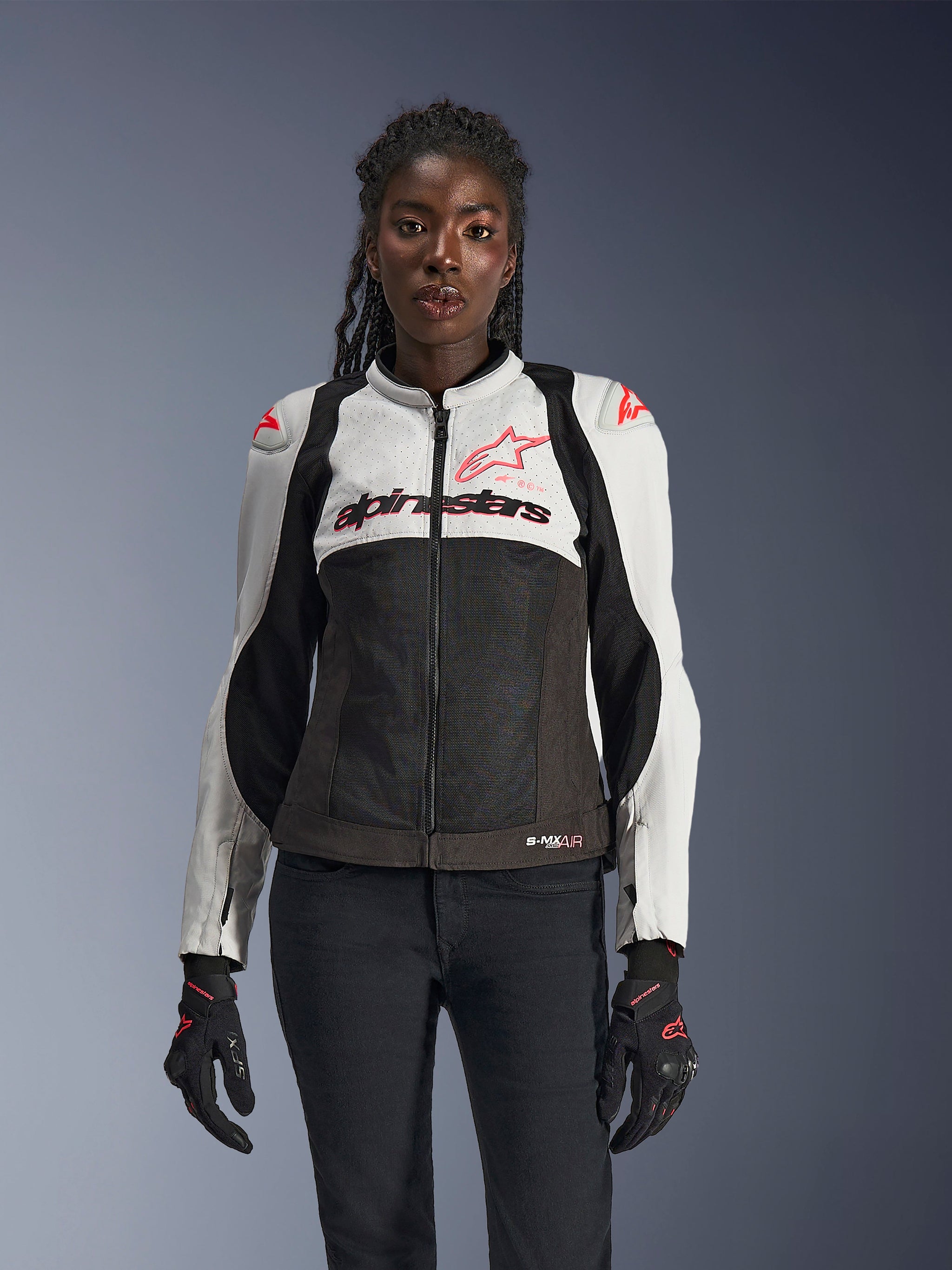 Alpinestars Woman Stella SMX Air Jacket, Ice Gray, Black, and Coral Fluo, featuring mesh construction and perforated panels, worn by a female model with black motorcycle gloves and pants, front view.