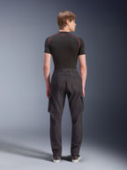 Calças Cargo Alpinestars Flex-AST, calças de motociclismo pretas, vista traseira no modelo, com um corte regular afunilado, bainhas elásticas e bolsos cargo laterais, combinadas com uma base layer preta e sapatilhas casuais