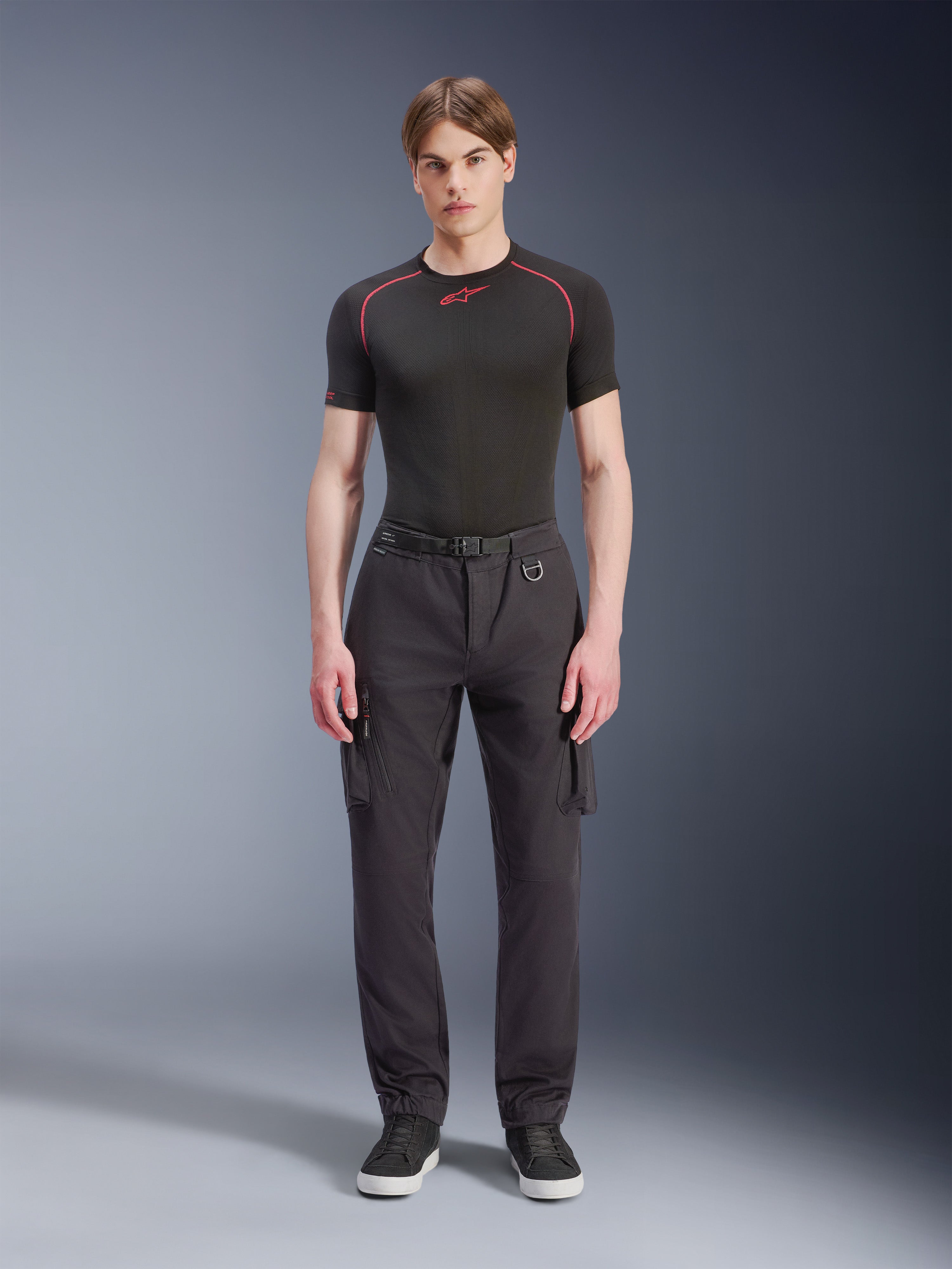 Alpinestars Flex-AST Cargo Pants, pretas, calças de motociclismo urbanas usadas por um modelo masculino com uma parte de cima de manga curta preta e sapatilhas, com um corte regular afunilado, bolsos cargo e pormenor de fivela de cinto integrada