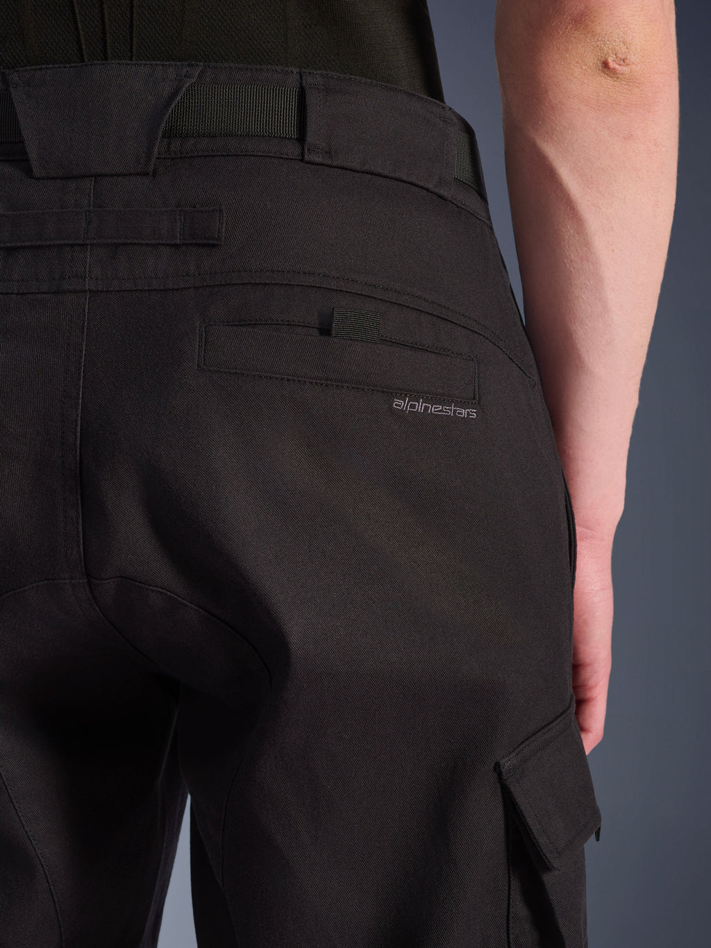 Calças Cargo Alpinestars Flex-AST, calças de motociclismo urbanas, pretas, grande plano da parte traseira e lateral mostrando o bolso traseiro com a marca Alpinestars, aba do bolso cargo lateral e construção em tecido elástico resistente.