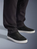 Alpinestars Flex-AST Cargo Pants, pretas, calças de motociclismo urbanas, vista de perto das pernas afuniladas e bainhas elásticas, combinadas com ténis pretos e brancos, tecido técnico de sarja de policotão para condução urbana casual