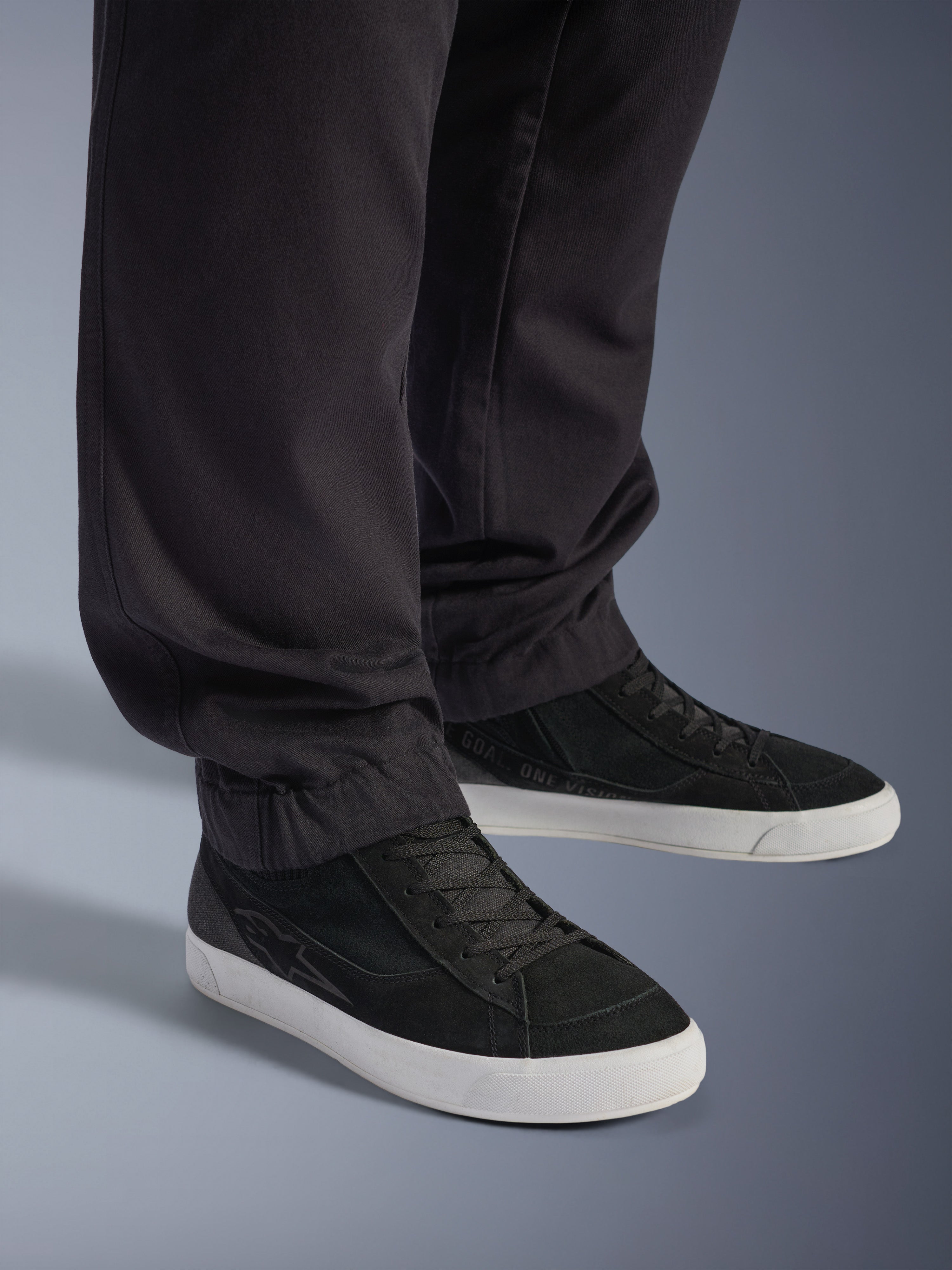 Alpinestars Flex-AST Cargo Pants, pretas, calças de motociclismo urbanas, vista de perto das pernas afuniladas e bainhas elásticas, combinadas com ténis pretos e brancos, tecido técnico de sarja de policotão para condução urbana casual