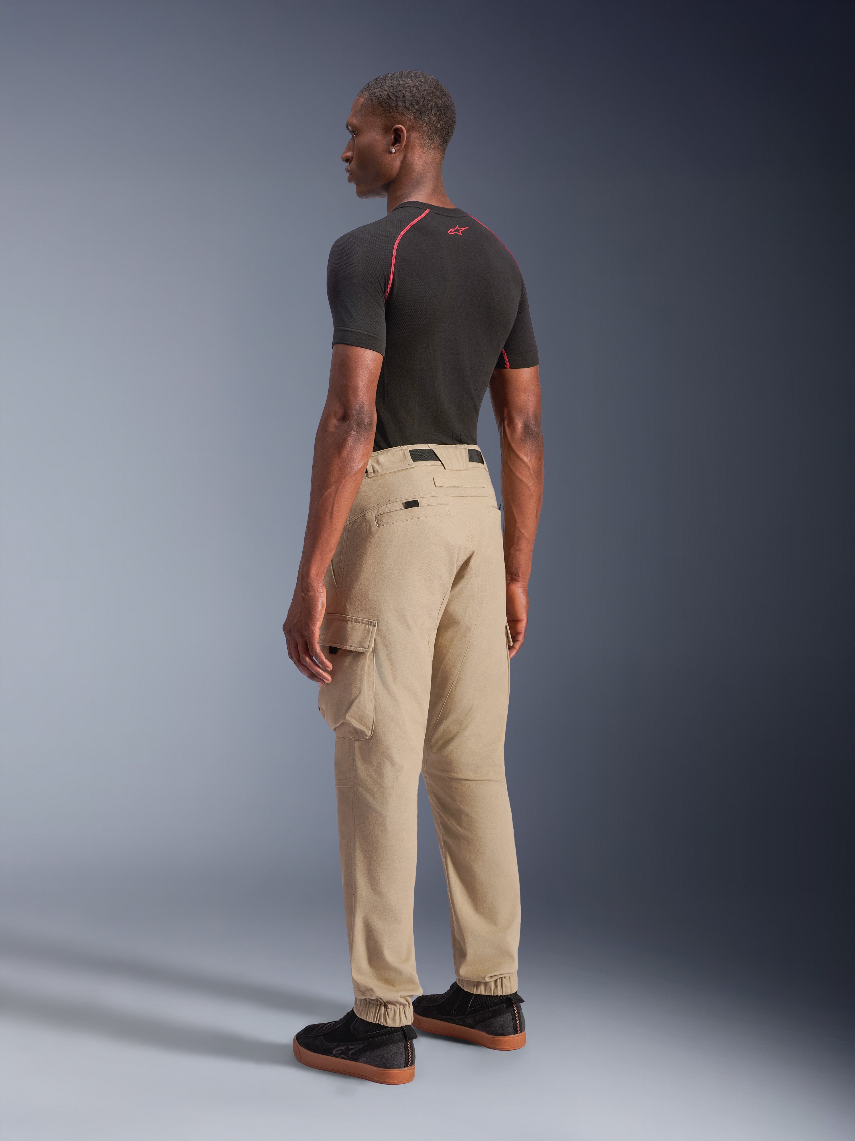 Alpinestars Flex-AST Cargo Pants - Short, Urban Motorcycle Pants in Light Beige, rear-quarter view showing side cargo pockets and elasticated hems, styled with a black short-sleeve top and black casual shoes