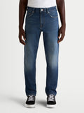 Alpinestars Flex-AST 8 Denim calças de ganga para moto para homem, azul médio, vista frontal num modelo a usar sapatilhas casuais, ganga de camada única com certificação AA
