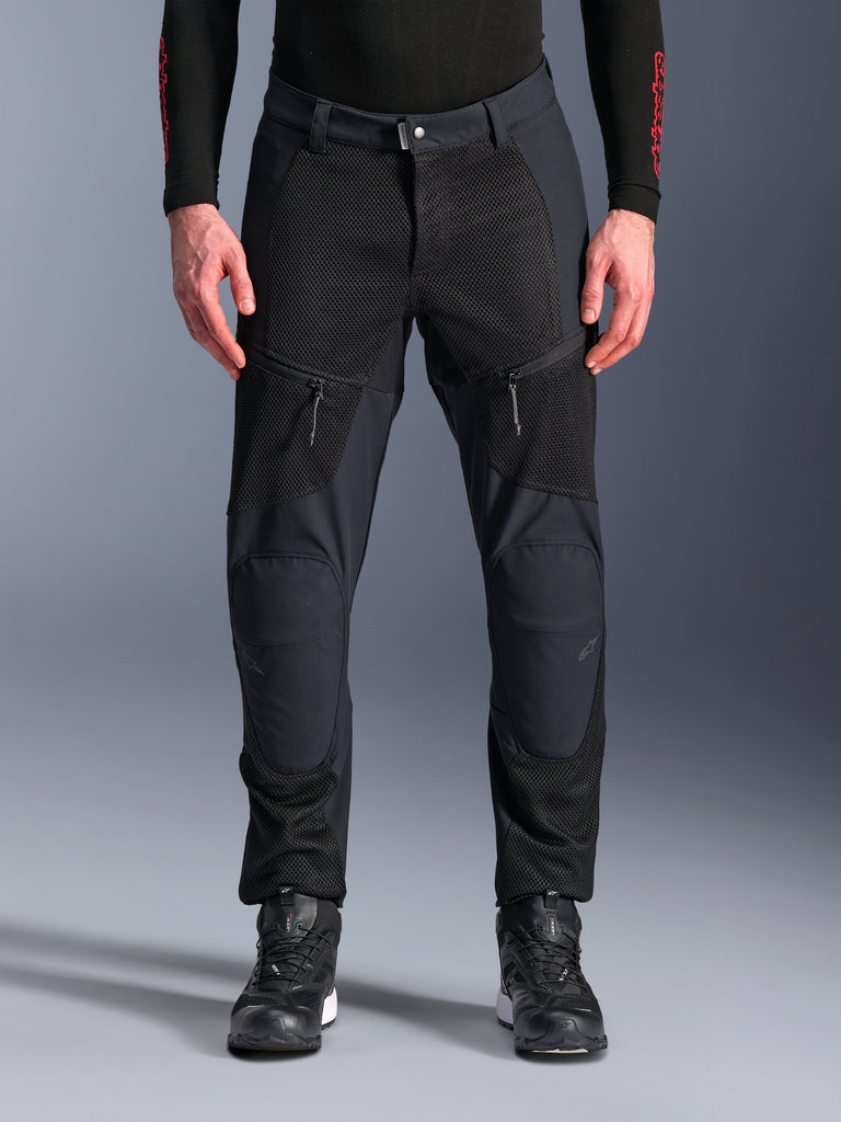 Alpinestars Troop-Air Pro Pants, calças de motociclismo pretas, com grandes painéis de ventilação em malha nas coxas e na parte inferior das pernas, bolsos frontais com fecho de correr, design têxtil com ajuste desportivo, usadas com sapatos de condução pretos e uma camada base de manga comprida