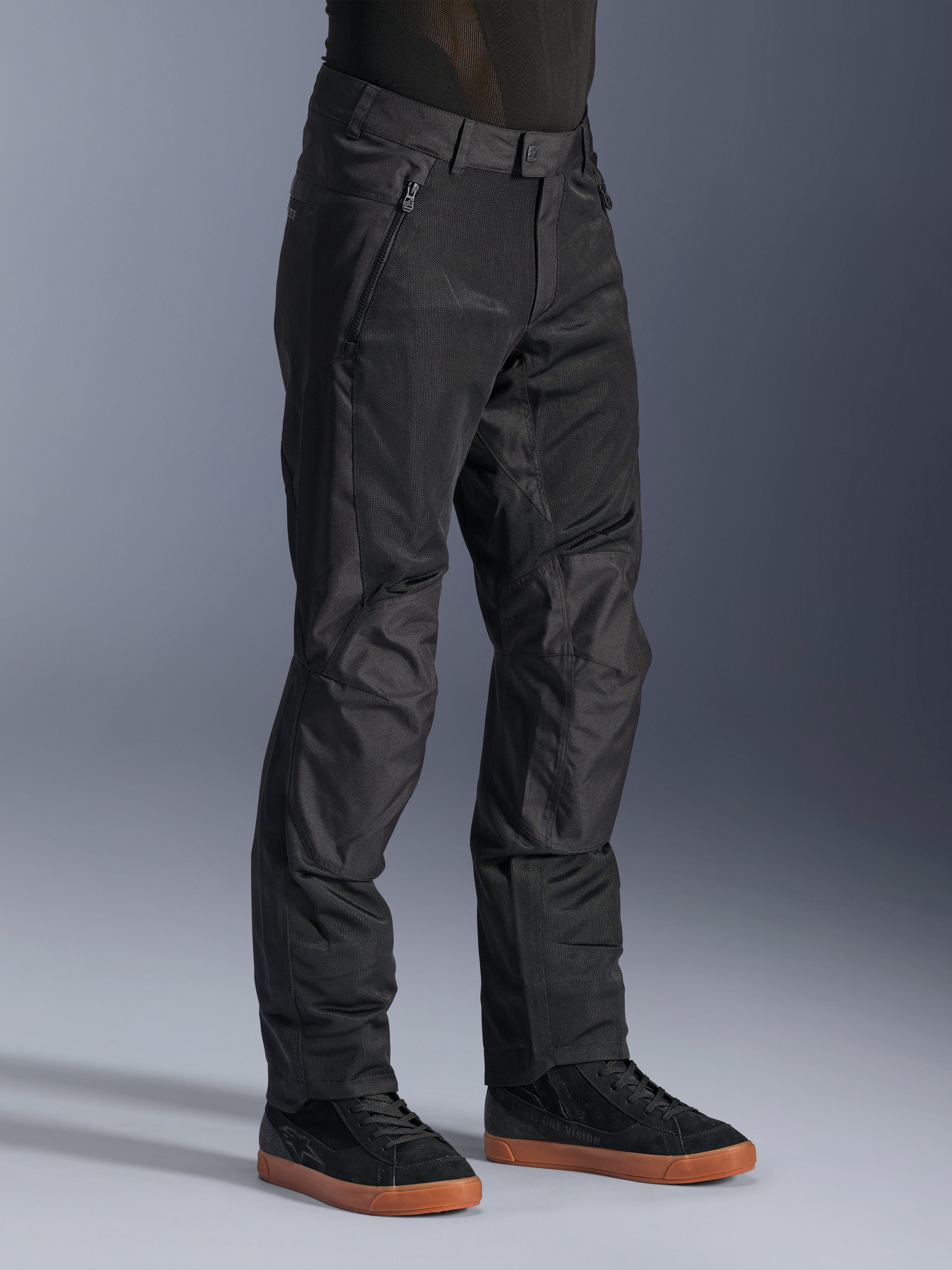 Calças Alpinestars C-1 Air, calças de motociclismo urbanas, pretas, com painéis de malha técnica respirável e construção em polifibra, usadas com sapatilhas pretas, design limpo e funcional para condução urbana.