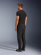 Alpinestars Aeroshell Airflow Pants, calças de motociclismo pretas, tecido softshell leve, usadas com uma t-shirt técnica de manga curta preta e botas de condução pretas, vista de perfil lateral traseira mostrando o corte justo e a construção ergonómica