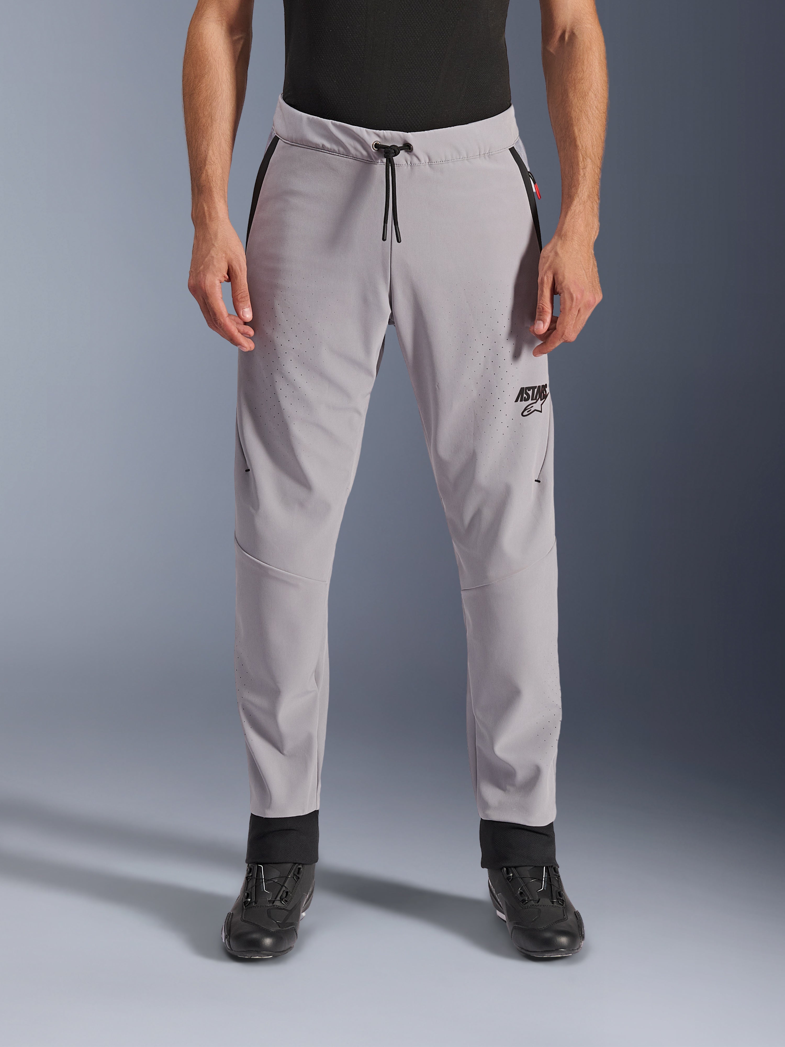 Calças Alpinestars Aeroshell Airflow, cinzento médio, vista frontal mostrando zonas perfuradas a laser nas coxas e canelas, cintura com cordão preto e logótipo ASTARS preto, chassis em softshell leve para condução em climas quentes