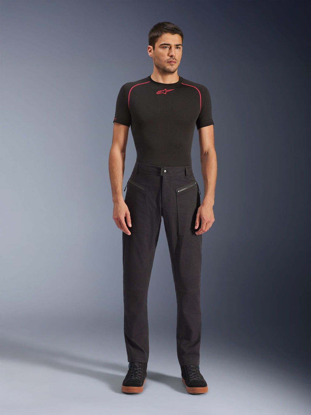 Alpinestars Flex-AST Canvas Pants, calças de motociclismo urbanas, pretas, usadas por um modelo com uma camisola interior de manga curta preta com costuras vermelhas e sapatilhas casuais pretas, destacando os bolsos frontais com fecho de correr e o design ergonómico em lona