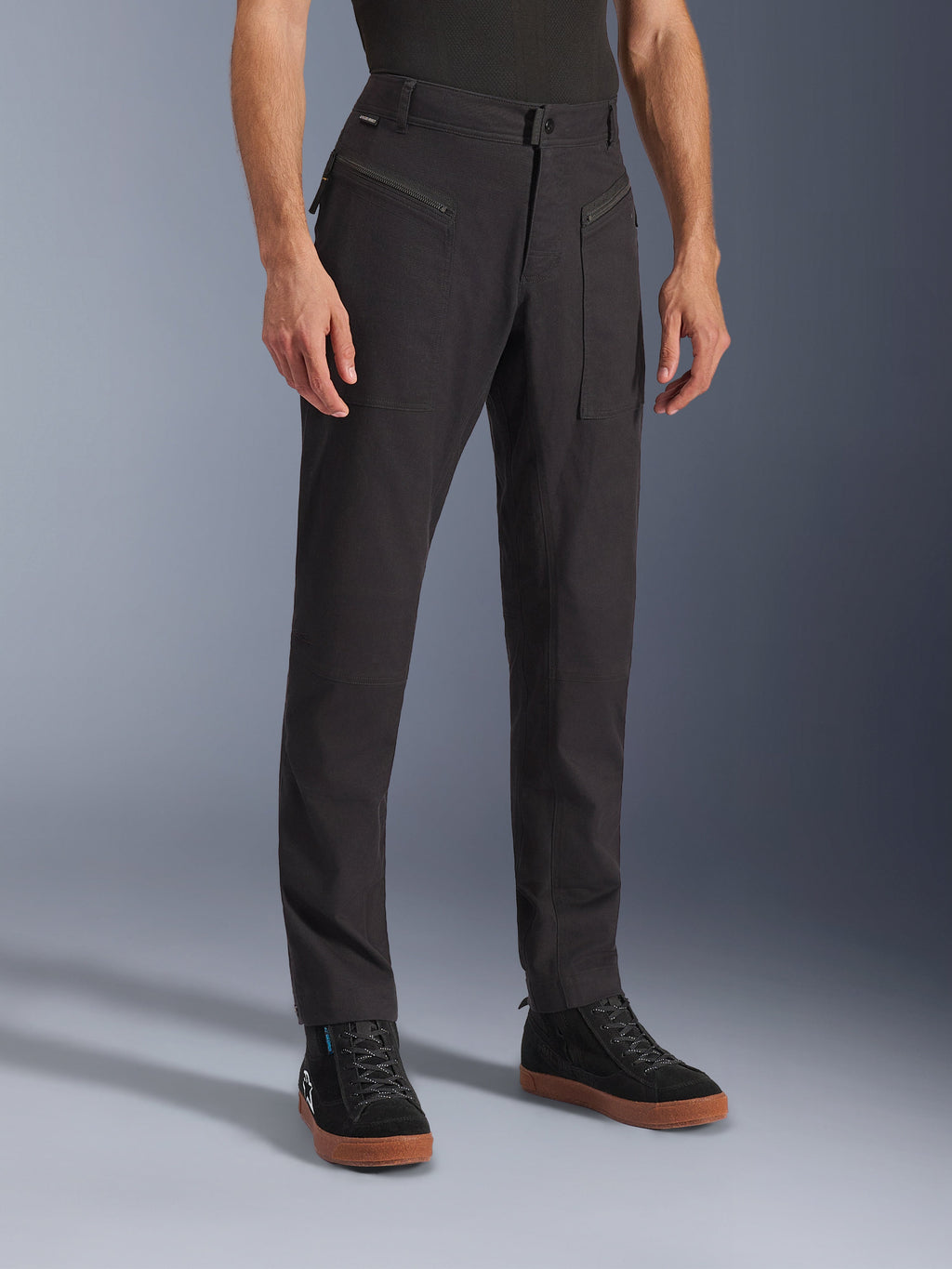 Alpinestars Flex-AST Canvas Pants, calças de motociclismo urbanas, pretas, usadas por um modelo com sapatilhas pretas, com um design clássico de roupa de trabalho, tecido de sarja de policotão elástico e bolsos frontais funcionais com fecho de correr
