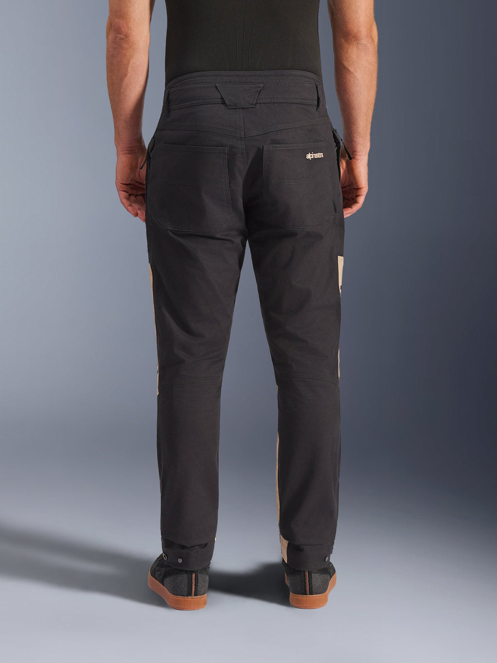 Alpinestars Flex-AST Canvas Pants em Black Aluminum, vista traseira mostrando o design utilitário com bolsos traseiros e detalhes laterais em bege, material de policotão elástico, equipamento de motociclismo urbano para homem.