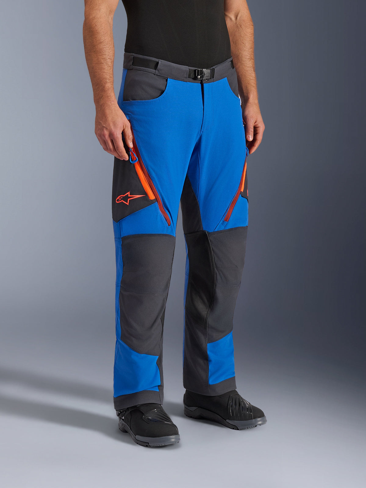 Alpinestars Maxdura Dual Pants, calças de motociclismo de aventura, Azul Royal e Cinzento Escuro com detalhes laranja, com aberturas de ventilação com fecho nas coxas, painéis reforçados nos joelhos e cinto com fivela magnética, design técnico sobre as botas para condução dual-sport.