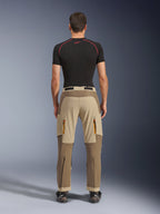 Alpinestars Maxdura Dual Pants em Walnut Aluminum, vista traseira com design em dois tons de castanho e bege, calças de aventura com bolsos cargo com fecho e assento reforçado, usadas com camisola de compressão preta e botas de motociclismo.