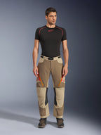 Alpinestars Maxdura Dual Pants, calças de aventura e dual-sport, cor Walnut Aluminum, usadas com uma camisola de compressão preta de manga curta e botas de aventura, com aberturas de ventilação cor-de-laranja com fecho e logótipos vermelhos nas coxas, cinto preto com fivela e design para usar por cima da bota para condução de motociclos.
