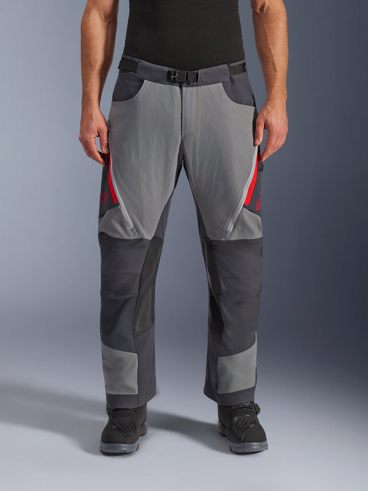 Alpinestars Maxdura Dual Pants, calças de motociclismo adventure, cinzento escuro e cinzento profundo com detalhes a vermelho, vista frontal mostrando aberturas de ventilação com fecho nas coxas, cinto com fivela magnética e painéis reforçados nos joelhos, design sobre a bota para condução dual-sport