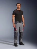 Alpinestars Maxdura Dual Pants, calças de motociclismo de aventura, cinzento escuro e cinzento profundo, usadas com uma camada base preta e botas, com aberturas de ventilação vermelhas com fecho de correr, painéis reforçados nos joelhos e assento, e cintura com cinto, corte atlético para condução dual-sport