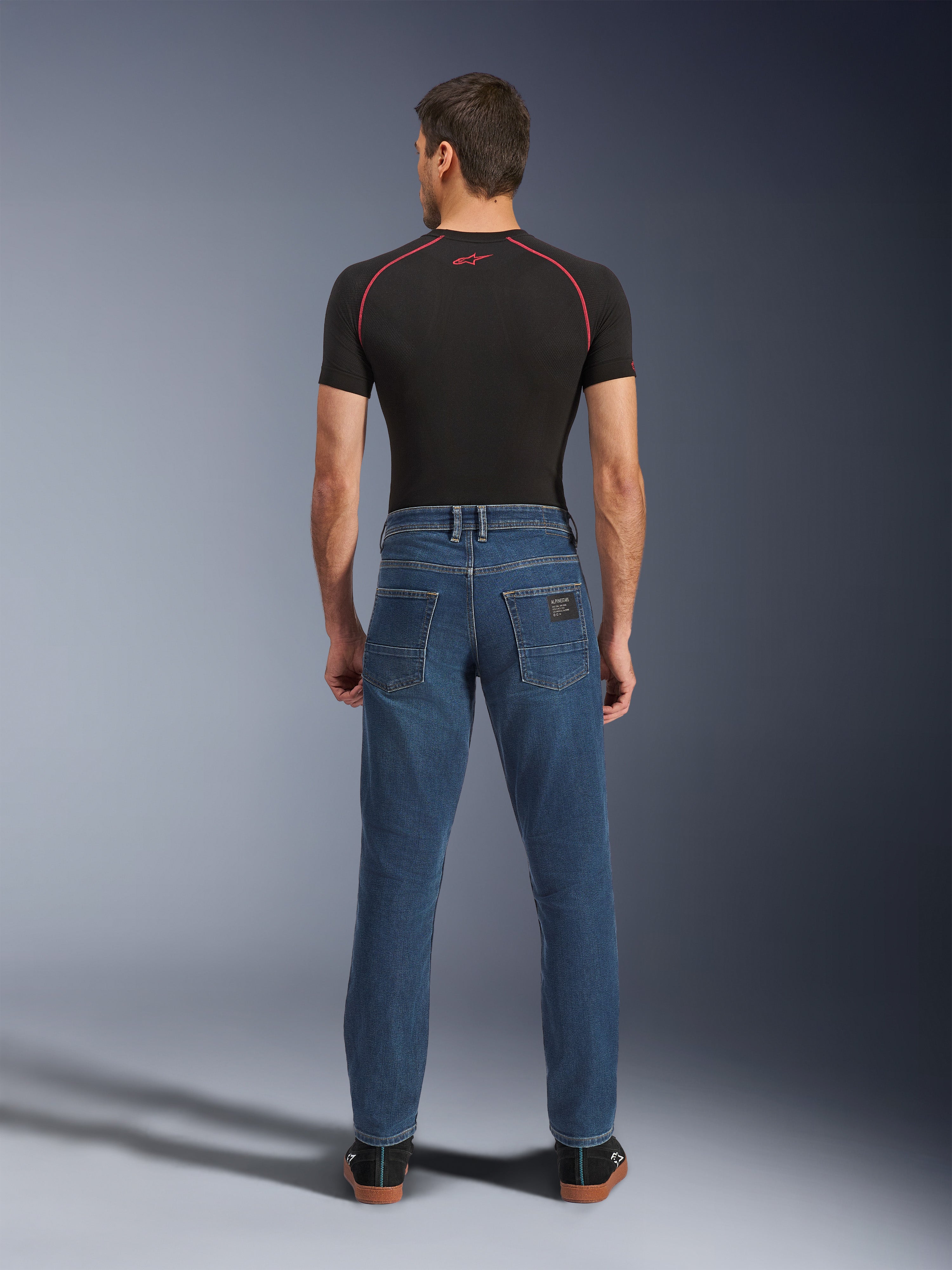Alpinestars Flex-AST 5 Denim Pants, Indigo Washed blue, rear view showing tapered urban fit, worn by model with black performance t-shirt and sneakers, casual motorcycle protective wear