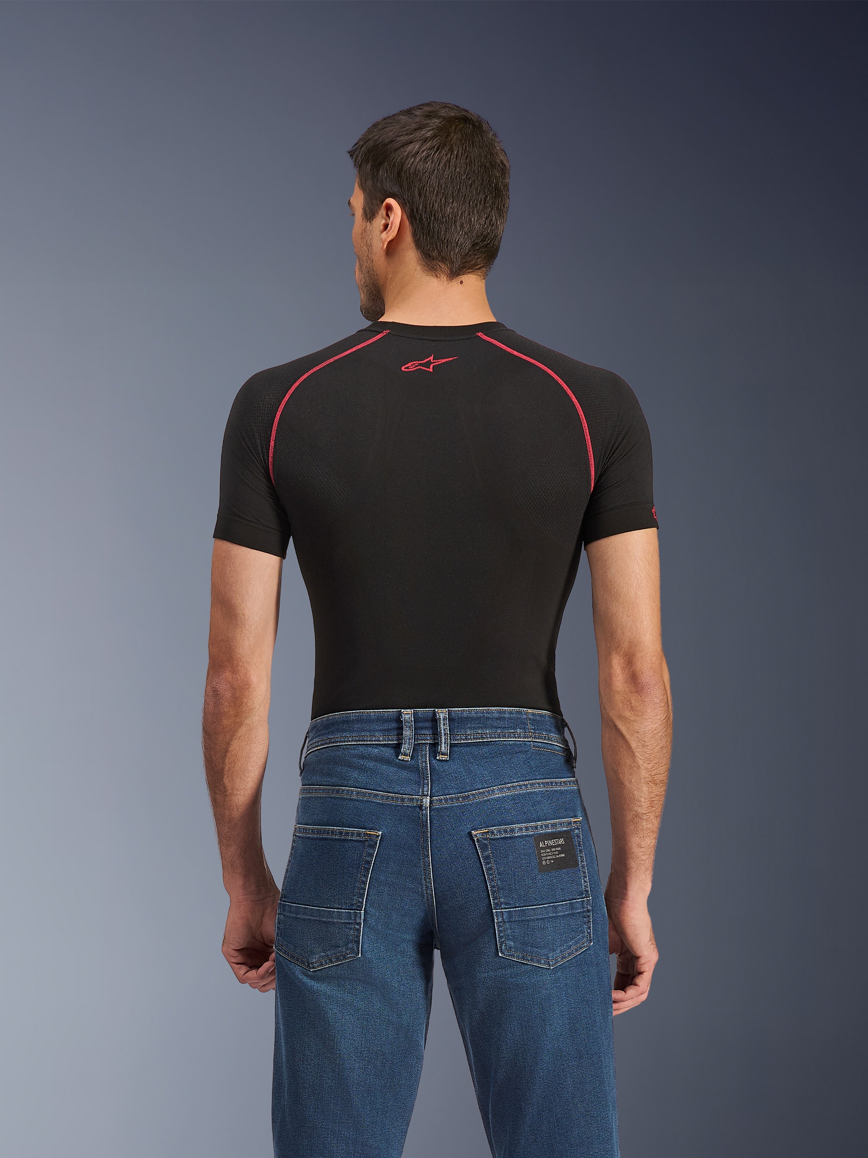 Alpinestars Flex-AST 5 Denim Pants, Indigo Washed, vista traseira a mostrar o corte regular afunilado, usadas com camada base preta de manga curta com costuras vermelhas, calças de ganga urbanas casuais para motociclismo