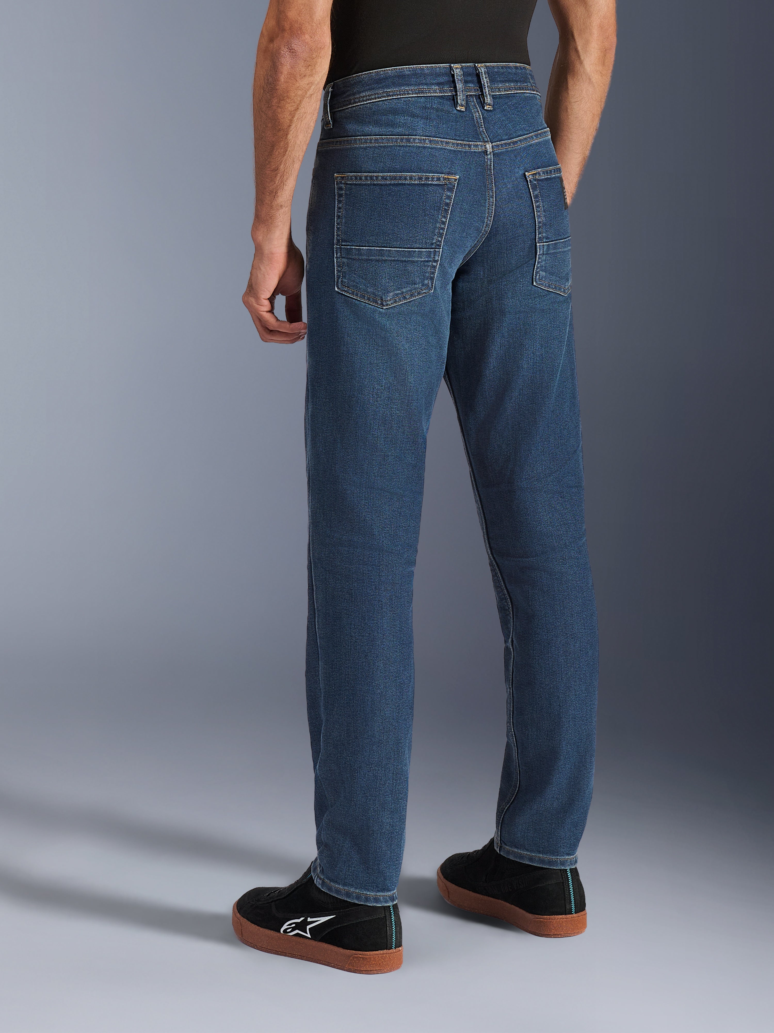 Alpinestars Flex-AST 5 Denim Pants, azul Indigo Washed, vista traseira de pessoa a usar calças de ganga casuais para motociclismo com um corte afunilado, combinadas com sapatilhas Alpinestars pretas, com bolsos traseiros e costuras reforçadas para condução urbana