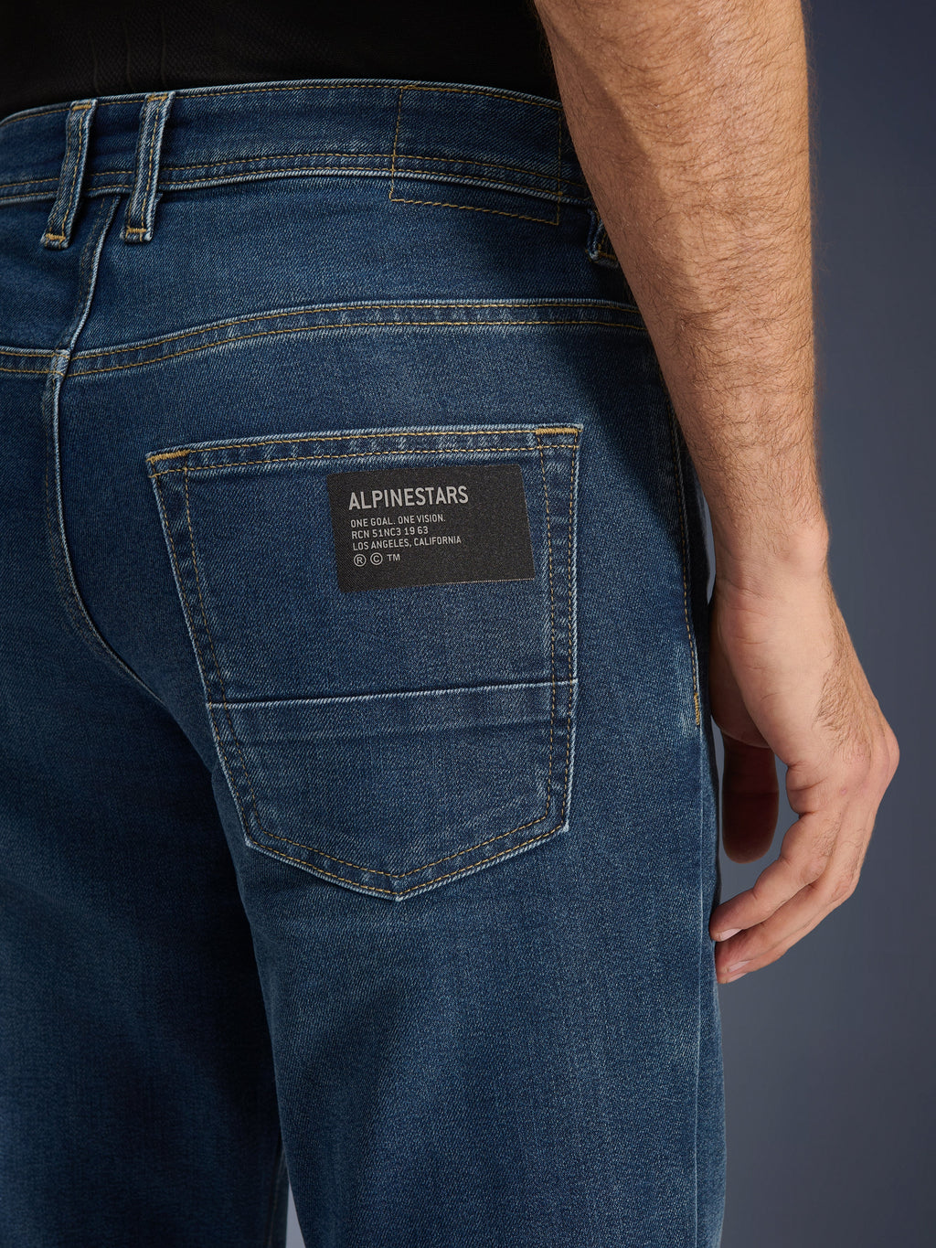 Alpinestars Flex-AST 5 Denim Pants, calças de ganga urbanas para motociclismo, Indigo Washed, grande plano do bolso traseiro apresentando um patch preto com o logótipo Alpinestars e o texto 'One Goal. One Vision.', costuras douradas contrastantes e textura de ganga de camada única