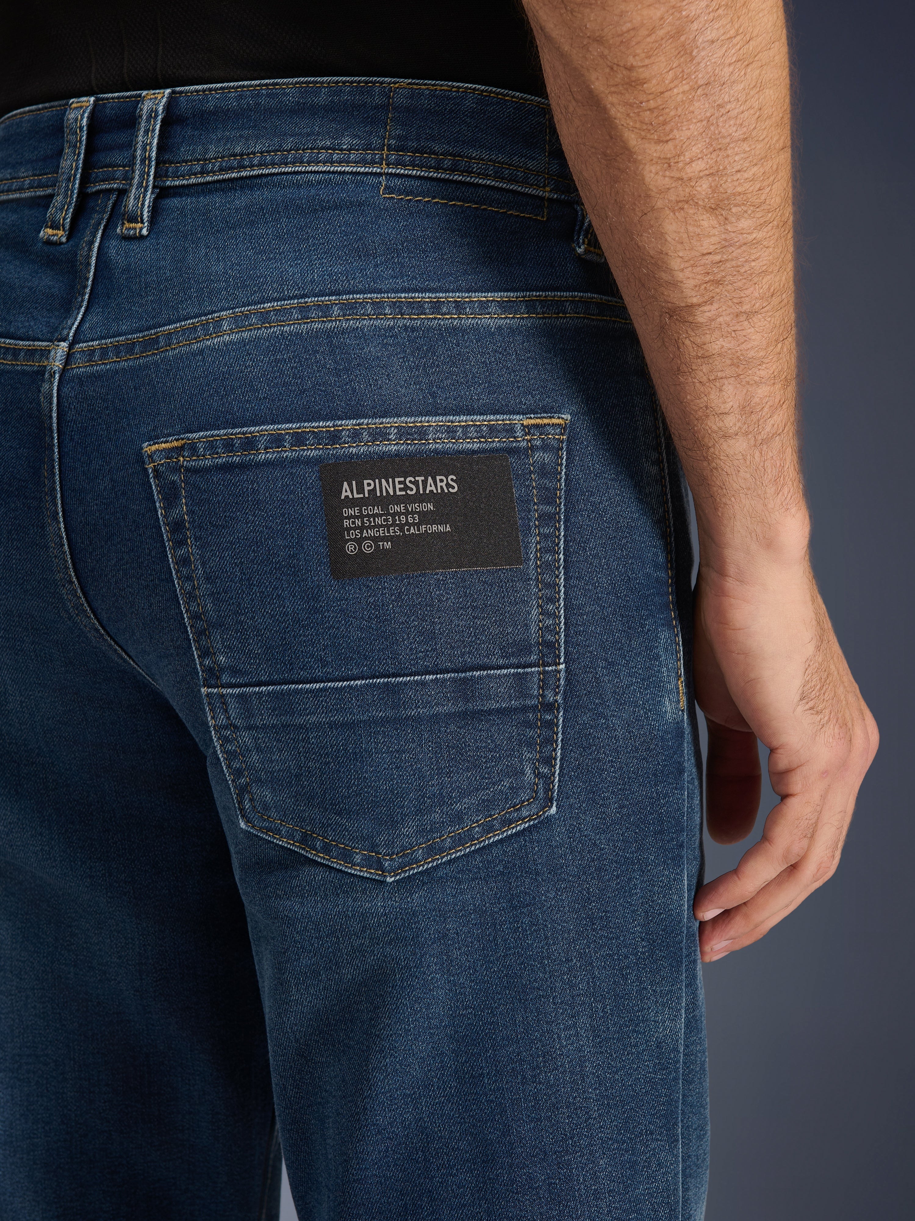 Alpinestars Flex-AST 5 Denim Pants, calças de ganga urbanas para motociclismo, Indigo Washed, grande plano do bolso traseiro apresentando um patch preto com o logótipo Alpinestars e o texto 'One Goal. One Vision.', costuras douradas contrastantes e textura de ganga de camada única