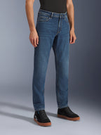 Calças Alpinestars Flex-AST 5 Denim, calças de ganga de motociclismo Indigo Washed, corte regular afunilado, usadas com sapatilhas de cano alto pretas e uma camisola preta, equipamento de condução urbana casual com um aspeto de ganga clássico.