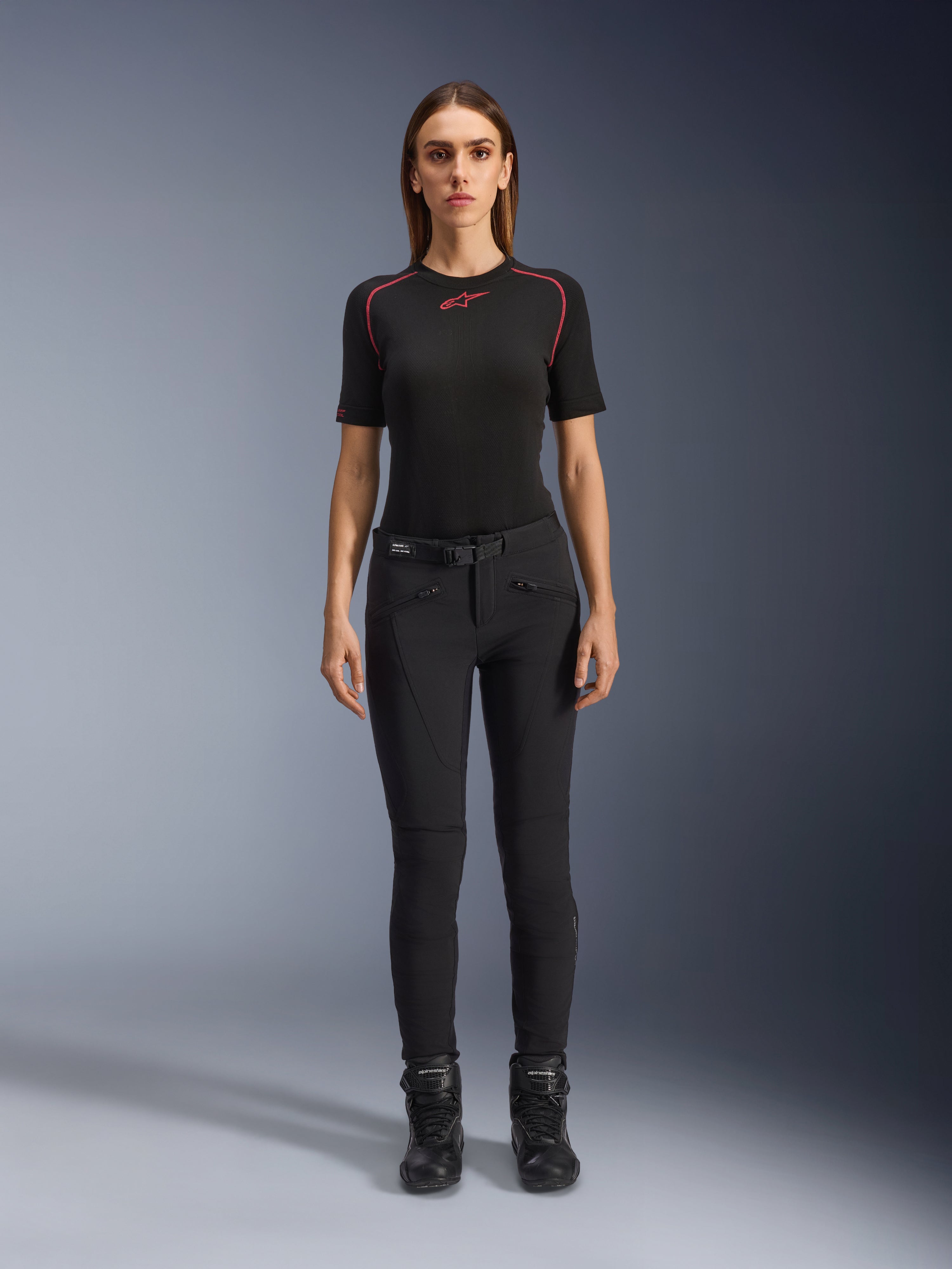Alpinestars Alamosa Women Pants, calças de motociclismo pretas de corte slim, apresentadas numa modelo virada para a frente, com bolsos frontais com fecho de correr e um cinto integrado na cintura, estilo minimalista inspirado no streetwear para condução urbana