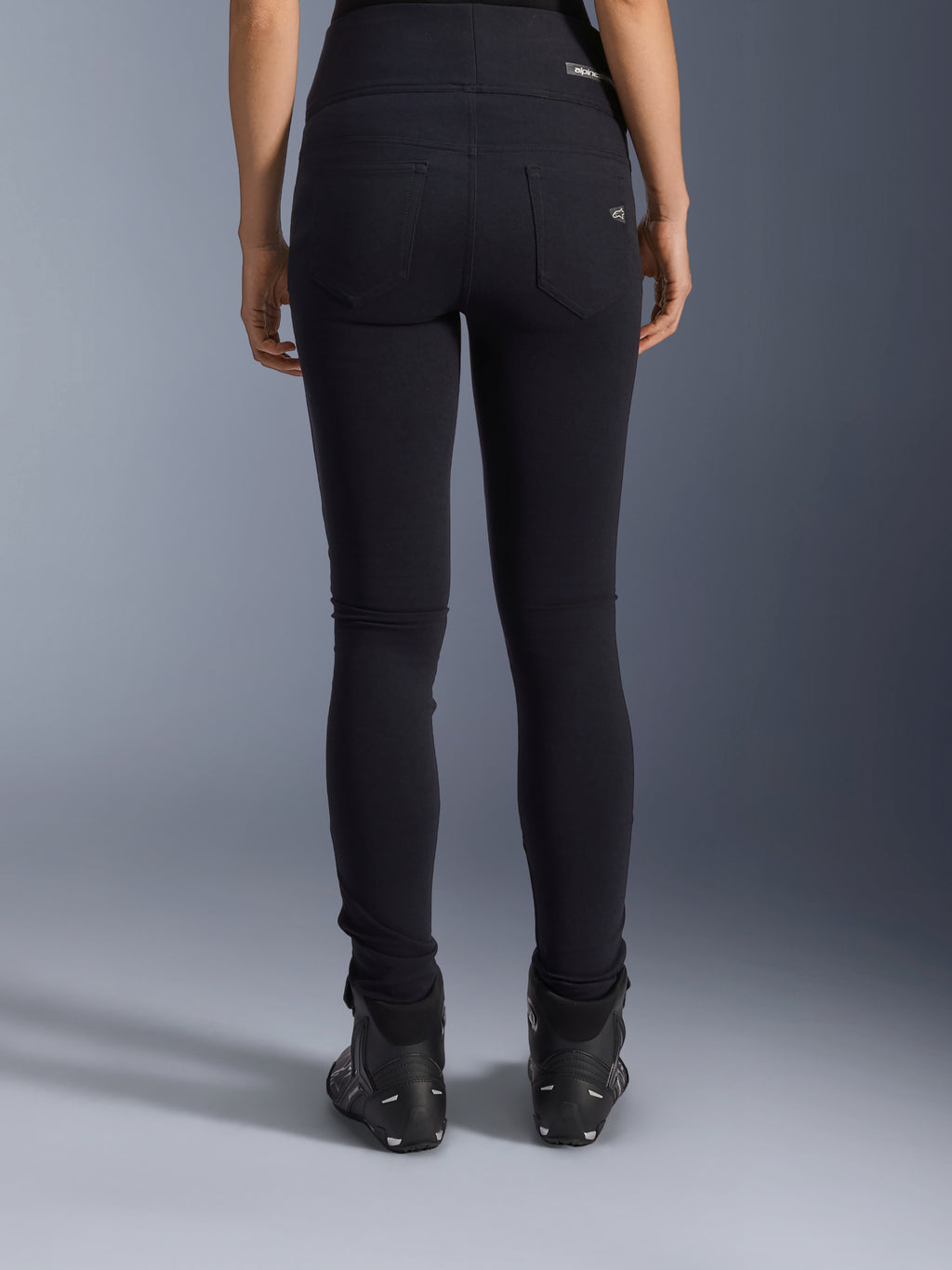 Alpinestars Stella Flex-Ast Leggings, leggings de motociclismo para mulher, pretas, vista traseira mostrando os bolsos e o ajuste justo, usadas com botas de motociclismo pretas, estilo de condução urbano