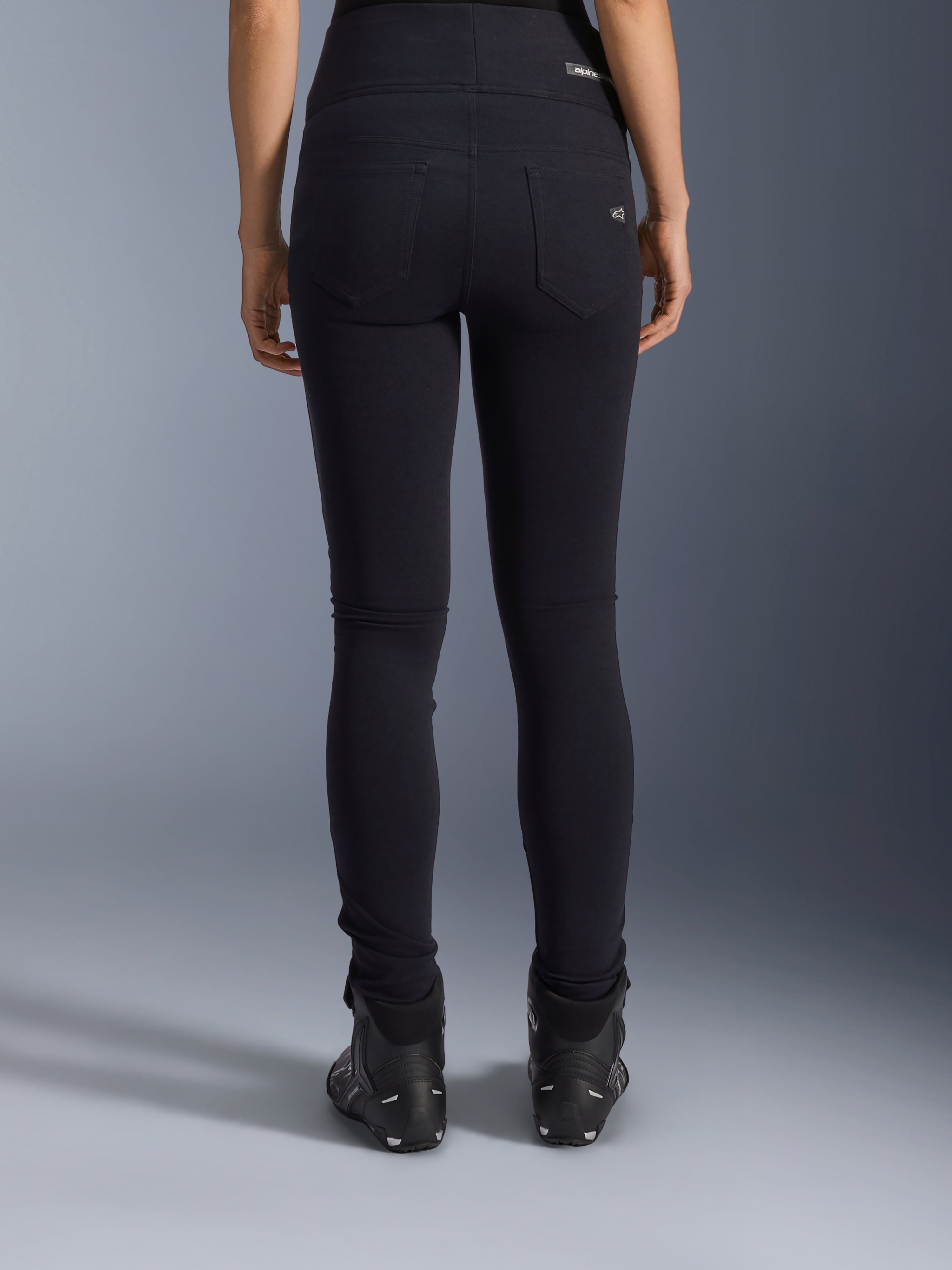 Alpinestars Stella Flex-Ast Leggings, leggings de motociclismo para mulher, pretas, vista traseira mostrando os bolsos e o ajuste justo, usadas com botas de motociclismo pretas, estilo de condução urbano