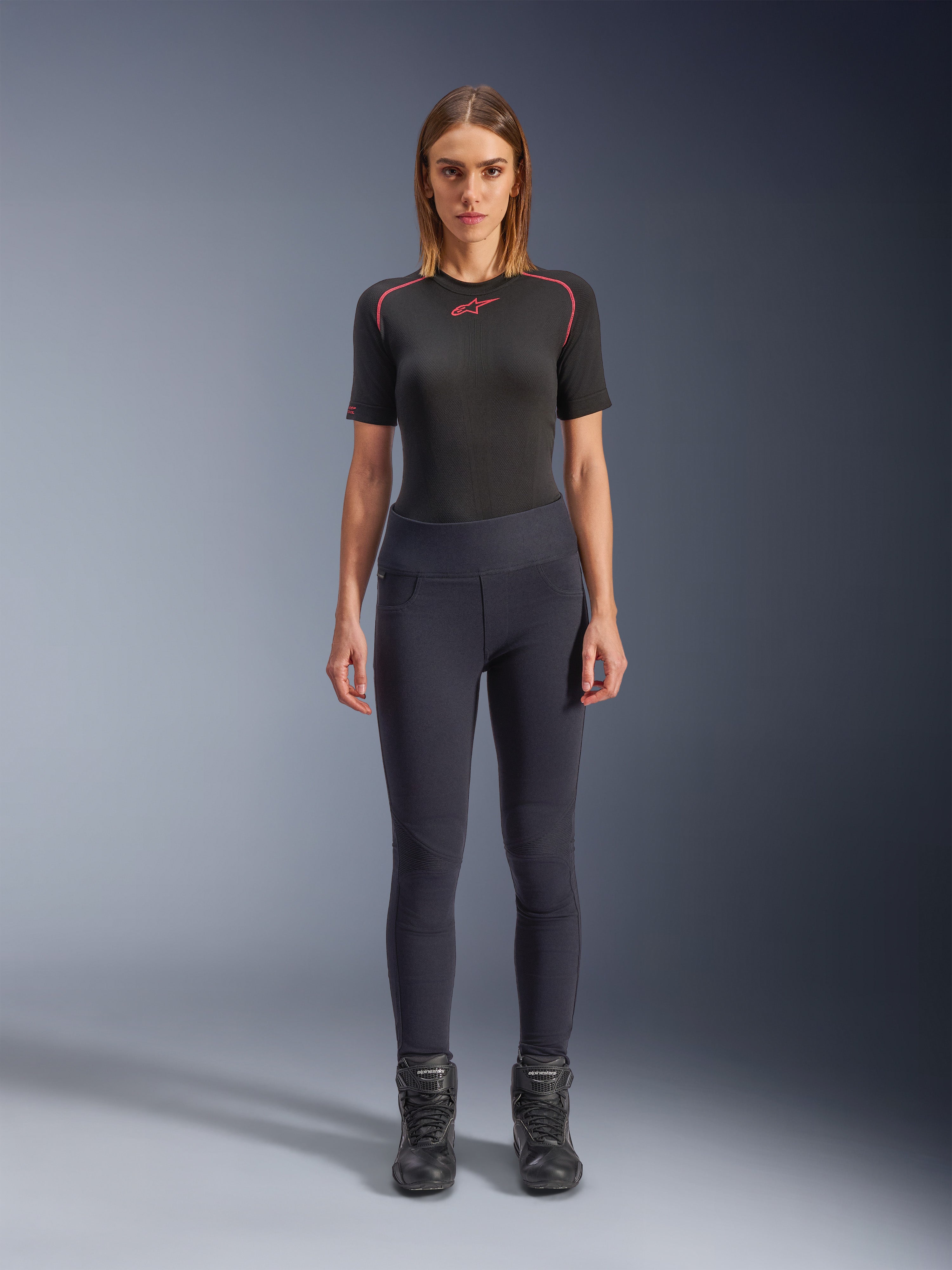 Alpinestars Stella Flex-Ast Leggings, leggings de motociclismo para mulher, pretas, usadas com um top preto de manga curta com detalhes vermelhos e botas de motociclismo pretas, equipamento de condução urbana contemporâneo de corte justo, vista frontal