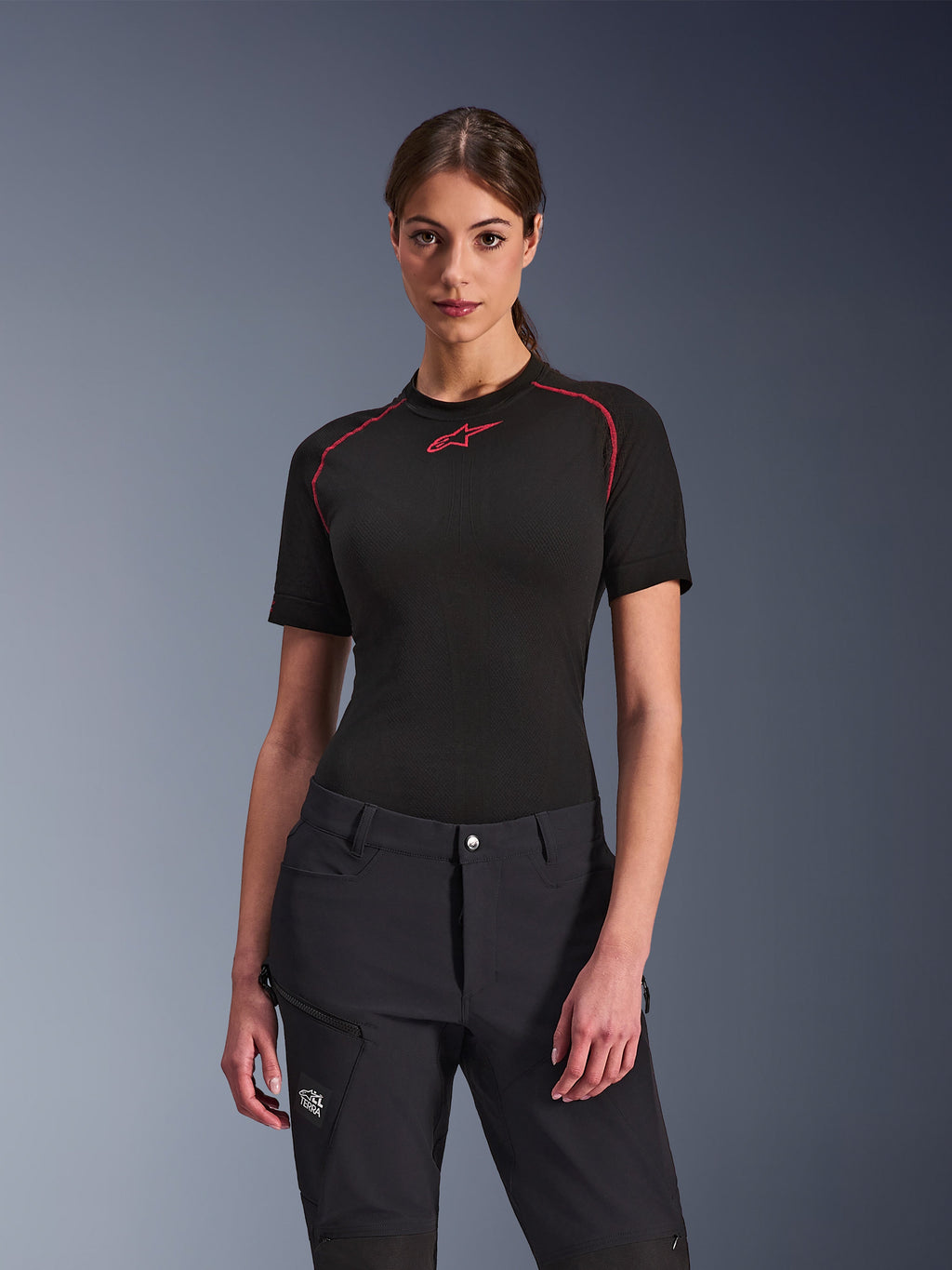 Mulher a usar calças Alpinestars Stella Flex-AST Explorer em preto, combinadas com uma camada base de manga curta preta com detalhes vermelhos, equipamento de condução de aventura com bolsos cargo e marca All Terra