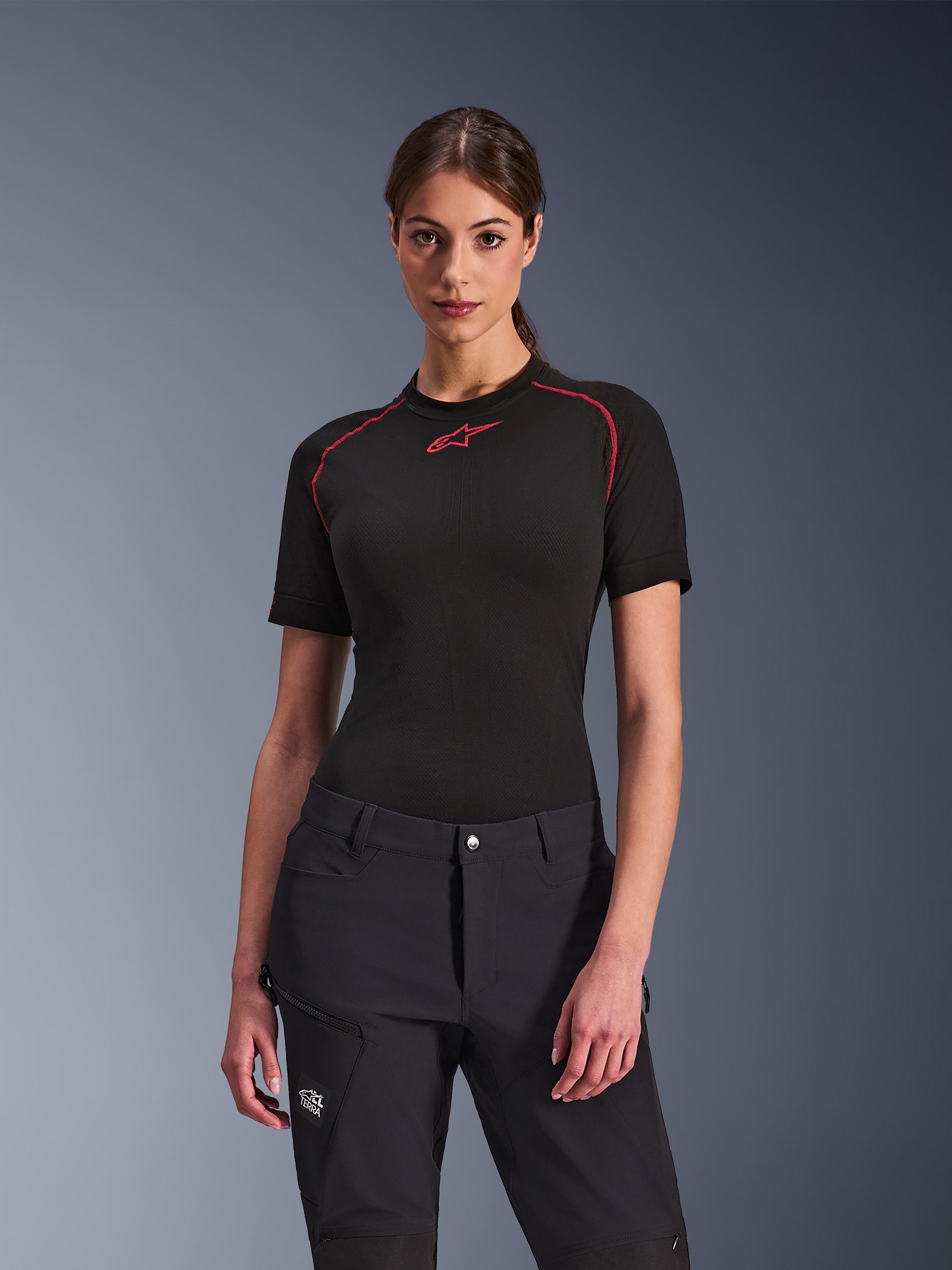 Mulher a usar calças Alpinestars Stella Flex-AST Explorer em preto, combinadas com uma camada base de manga curta preta com detalhes vermelhos, equipamento de condução de aventura com bolsos cargo e marca All Terra