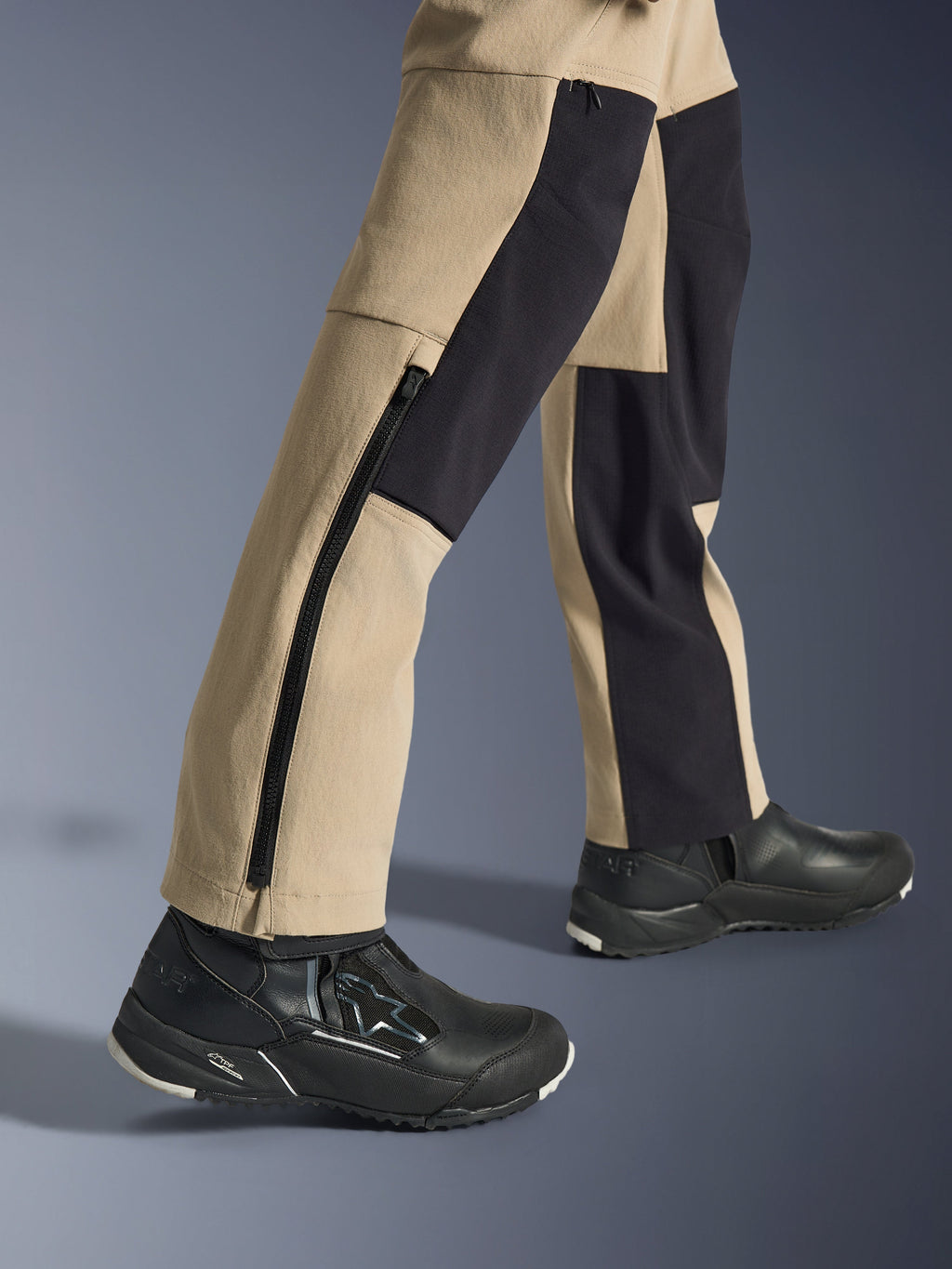 Calças Alpinestars Stella Flex-AST Explorer para Mulher, calças de aventura para motociclismo, areia e preto, vista aproximada da parte inferior das pernas e tornozelos com um fecho de correr lateral longo e painéis de reforço pretos, usadas com sapatos de condução Alpinestars pretos.