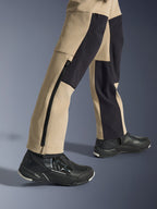 Calças Alpinestars Stella Flex-AST Explorer para Mulher, calças de aventura para motociclismo, areia e preto, vista aproximada da parte inferior das pernas e tornozelos com um fecho de correr lateral longo e painéis de reforço pretos, usadas com sapatos de condução Alpinestars pretos.