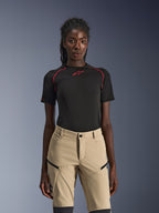 Calças Alpinestars Stella Flex-AST Explorer, calças de motociclismo para mulher em cor areia, usadas com um top técnico de manga curta preto com costuras vermelhas, equipamento de touring de aventura com bolsos cargo com fecho e tecido ripstop resistente.