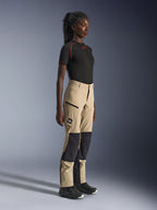 Calças Alpinestars Stella Flex-AST Explorer para Mulher, calças de aventura e touring em areia e preto, perfil lateral de uma modelo a usar uma t-shirt preta Alpinestars e botas de motociclismo, com reforços de ripstop nos joelhos e bolsos cargo com fecho de correr.