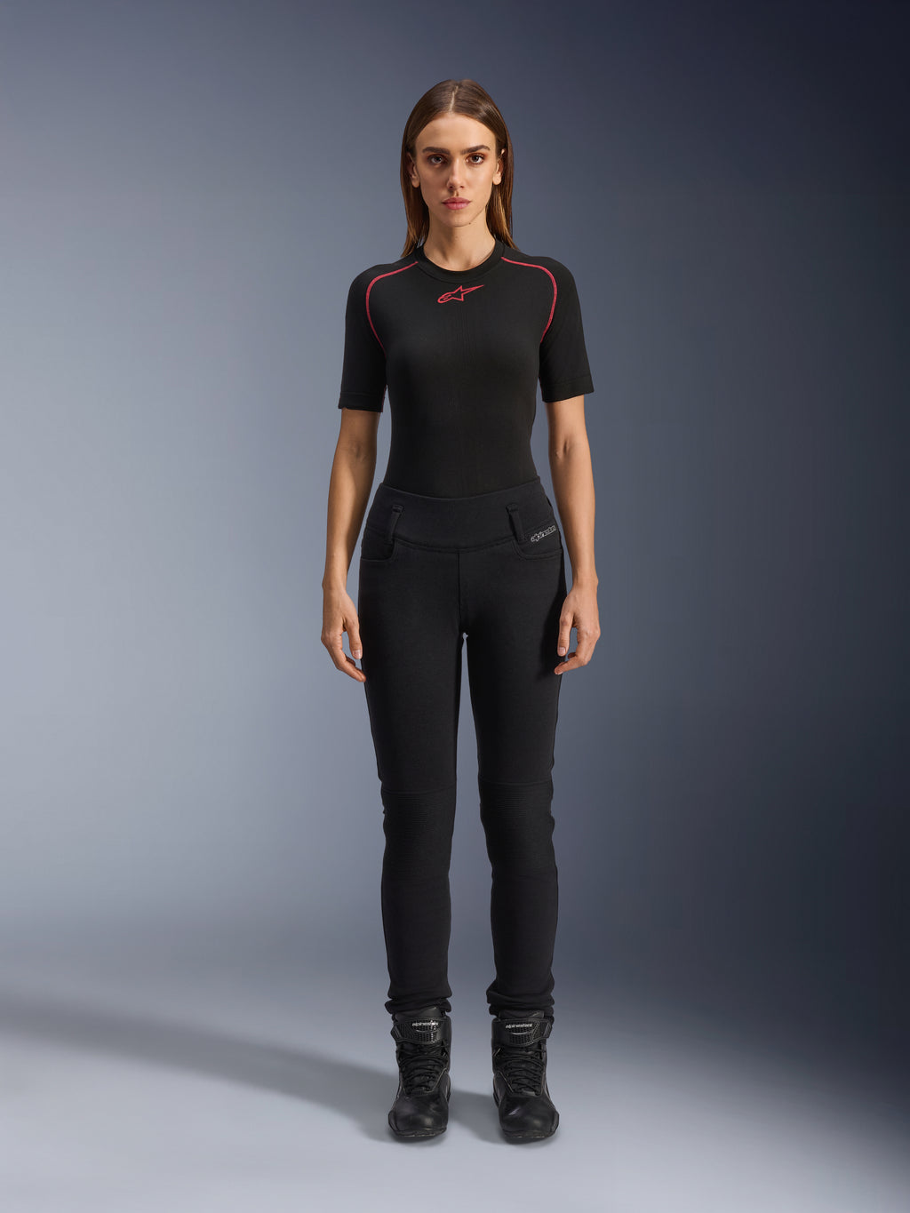 Alpinestars Womens Banshee Leggings, leggings de motociclismo pretas, ajuste anatómico que se molda ao corpo, usadas por uma modelo feminina com uma camada de base preta e botas de motociclismo, com painéis canelados nos joelhos e cintura subida para condução urbana.