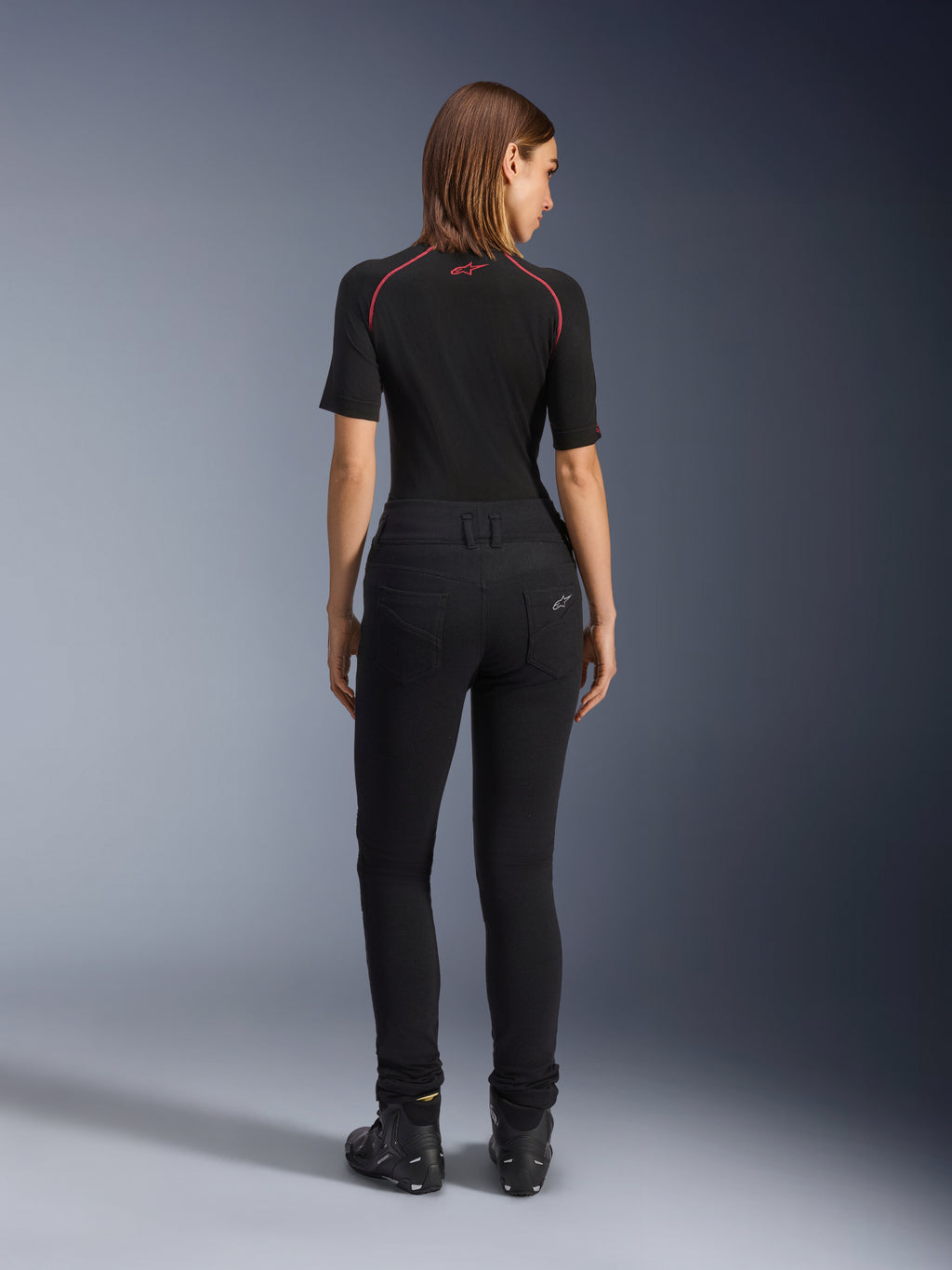 Leggings Femininas Alpinestars Banshee, leggings de motociclismo pretas, vista traseira realçando o ajuste justo ao corpo e o tecido elástico anatómico, com bolsos traseiros e detalhe do logótipo, usadas com uma camada de base preta e sapatos de condução, equipamento de motociclismo urbano para mulher