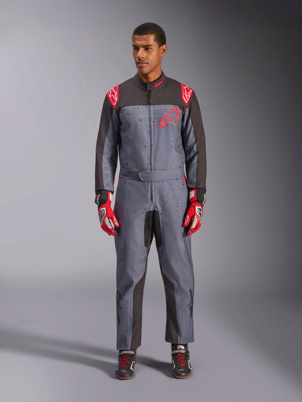 Fato Alpinestars KMX-9 V3 Graphic 6, fato de karting, preto antracite e vermelho, padrão gráfico salpicado a cinzento, painéis pretos na parte interior dos braços e pernas, logótipos Alpinestars vermelhos nos ombros e no peito, usado com luvas de competição vermelhas e sapatos pretos
