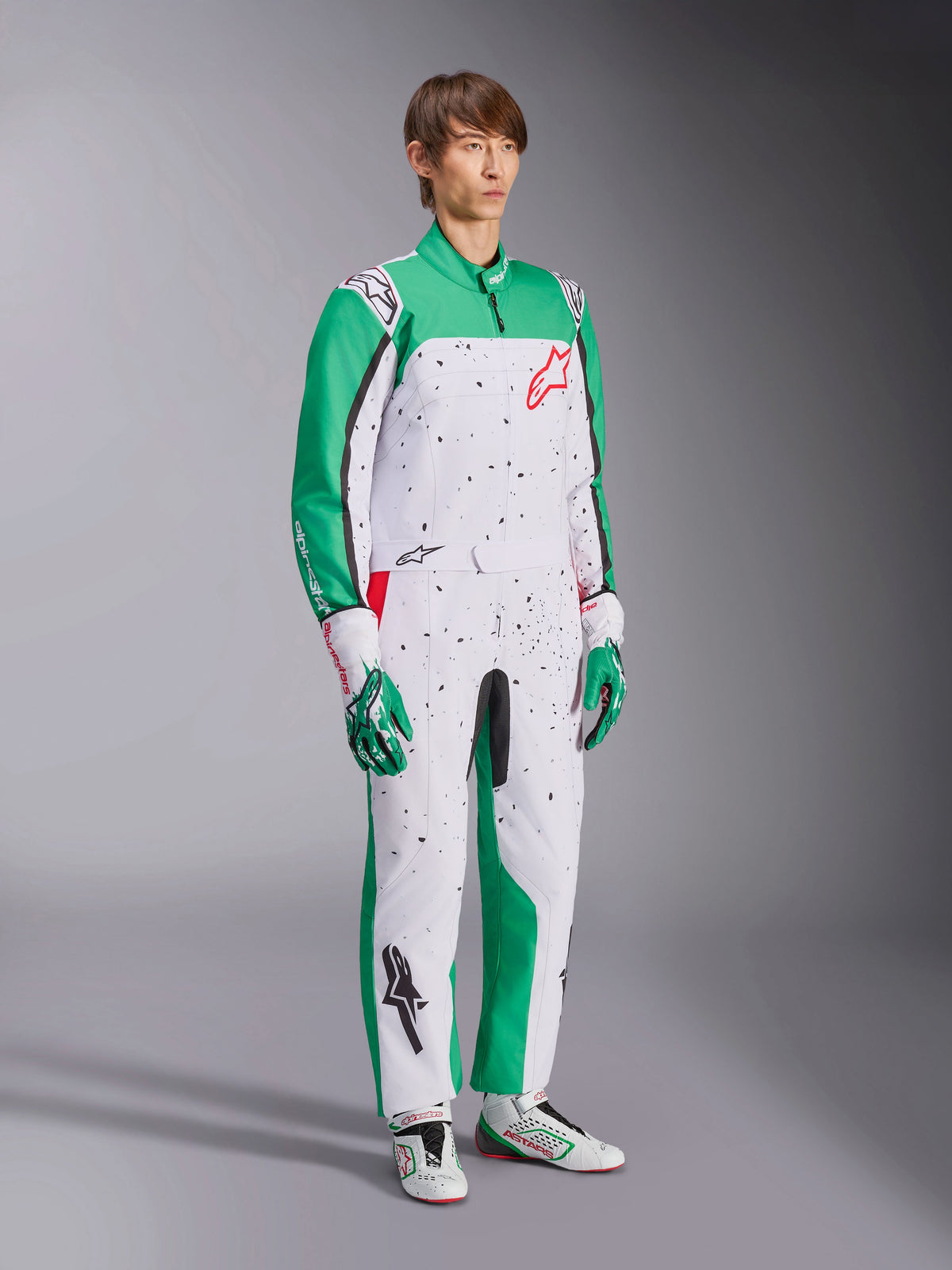 Fato Alpinestars KMX-9 V3 Graphic 6, fato de karting, branco, verde e vermelho, usado com luvas e sapatos de corrida a condizer, apresenta um corpo branco com mangas verdes e grafismos de salpicos pretos, logótipo Alpinestars vermelho no peito, design atlético de peça única para desportos motorizados
