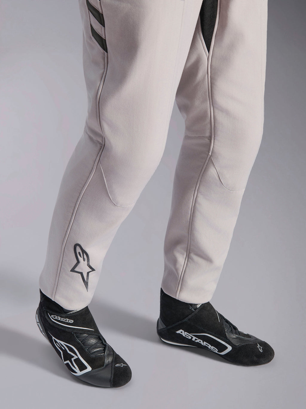 Fato Alpinestars GP Race V3 FIA, fato de automobilismo Silver Anthracite, detalhe da parte inferior das pernas e botas de corrida pretas, com o logótipo Astars preto na perna, equipamento profissional de desporto motorizado com punhos canelados