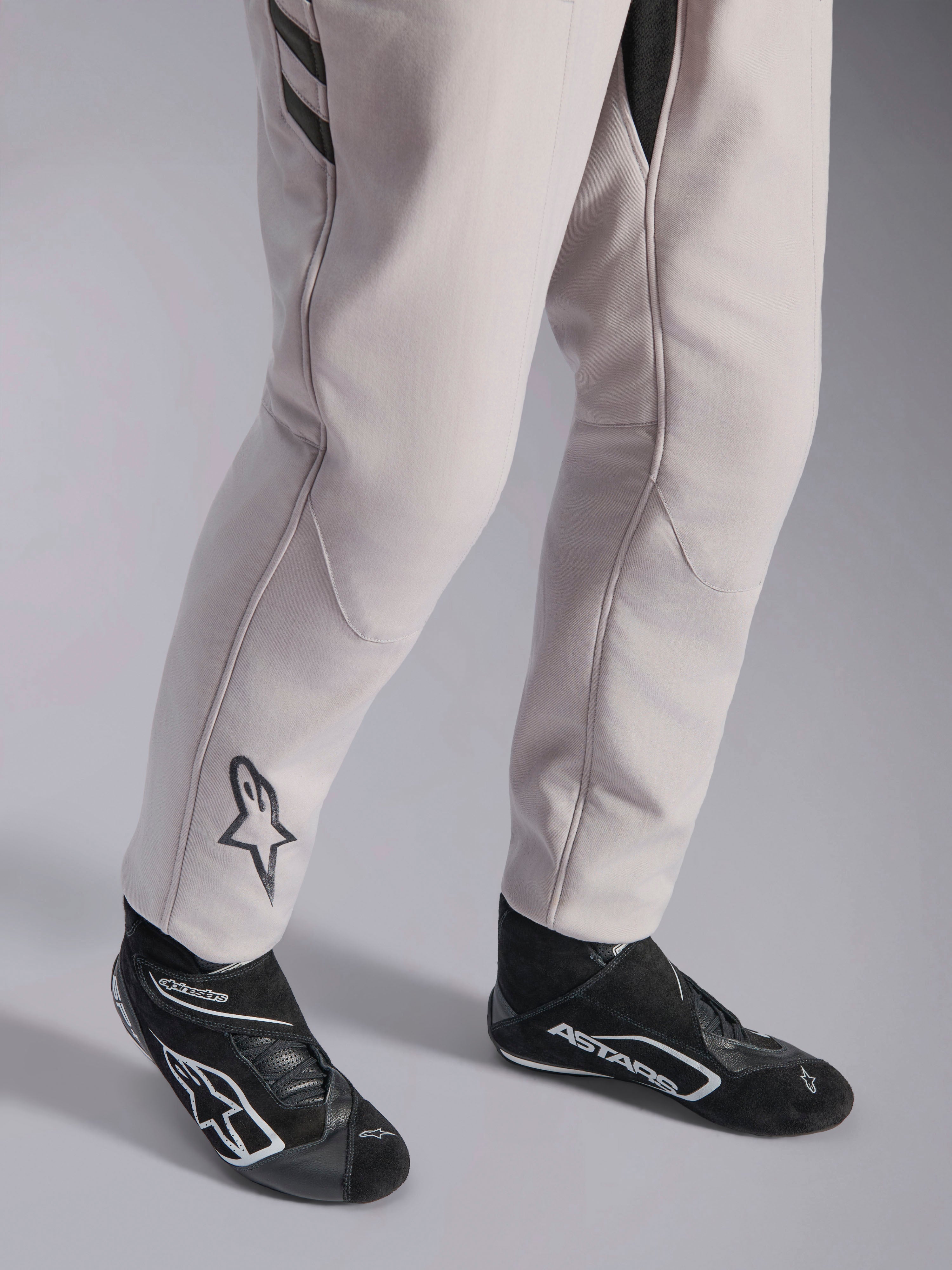 Fato Alpinestars GP Race V3 FIA, fato de automobilismo Silver Anthracite, detalhe da parte inferior das pernas e botas de corrida pretas, com o logótipo Astars preto na perna, equipamento profissional de desporto motorizado com punhos canelados