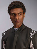 Macacão Alpinestars GP Race V3 FIA, fato de automobilismo preto usado por um homem, vista de perto com foco no colarinho macio e logótipos de estrela brancos nas ombreiras, equipamento de proteção profissional para desportos motorizados