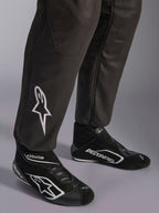 Macacão Alpinestars GP Race V3 FIA, grande plano da parte inferior das pernas e botas de competição, preto com detalhes prateados, com logótipo de estrela bordado a branco na canela e punhos canelados nos tornozelos, equipamento de proteção profissional para automobilismo