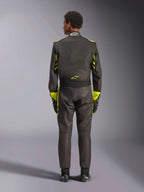 Fato Alpinestars GP Race V3 FIA, vista traseira, preto com detalhes em amarelo néon, apresentando painéis amarelos nos braços e no tronco, logótipo amarelo na parte inferior das costas, usado com luvas e botas de corrida a condizer, fato de corrida automóvel profissional.