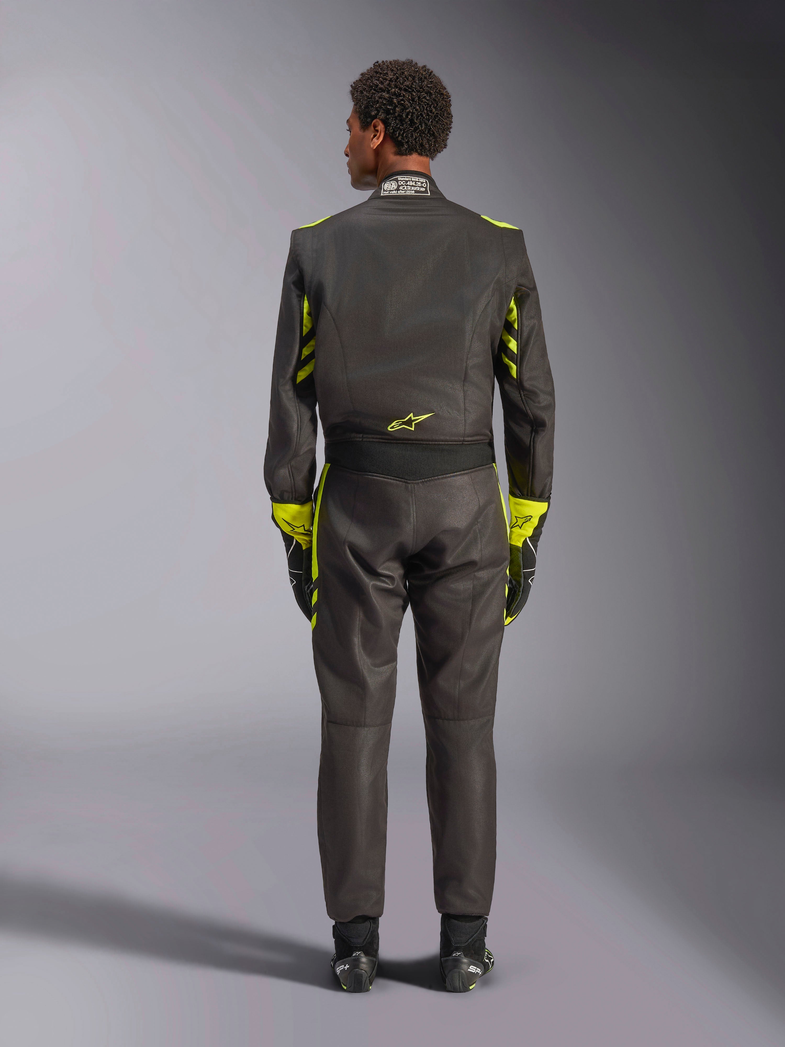 Fato Alpinestars GP Race V3 FIA, vista traseira, preto com detalhes em amarelo néon, apresentando painéis amarelos nos braços e no tronco, logótipo amarelo na parte inferior das costas, usado com luvas e botas de corrida a condizer, fato de corrida automóvel profissional.